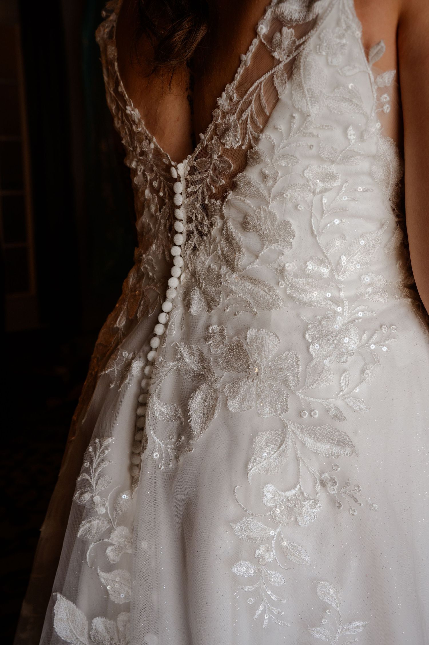 Intricate white lace and beaded details adorn the bodice of a wedding dress against a dark background.