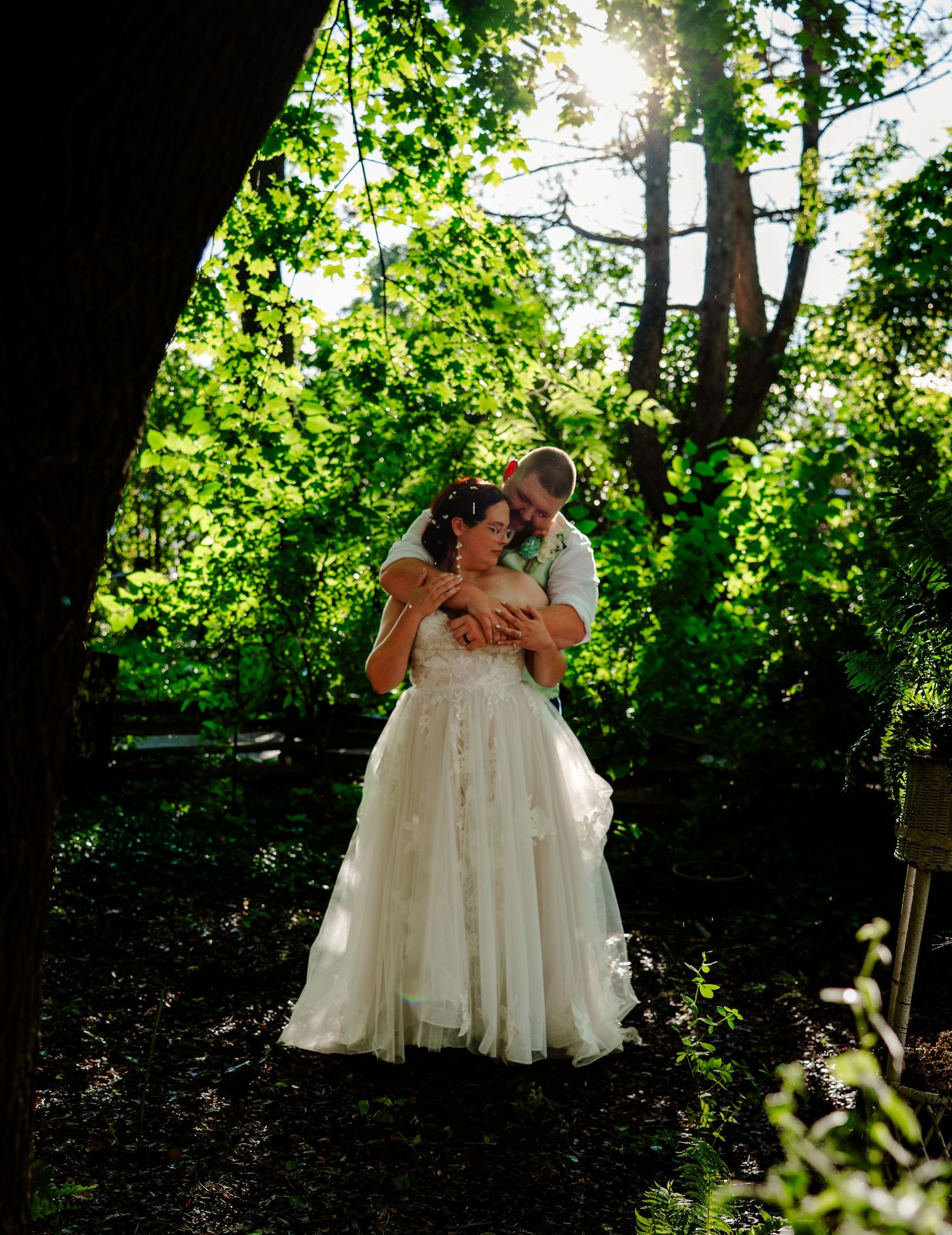 Two figures in white lacy dresses share an intimate moment in a sunlit garden setting.