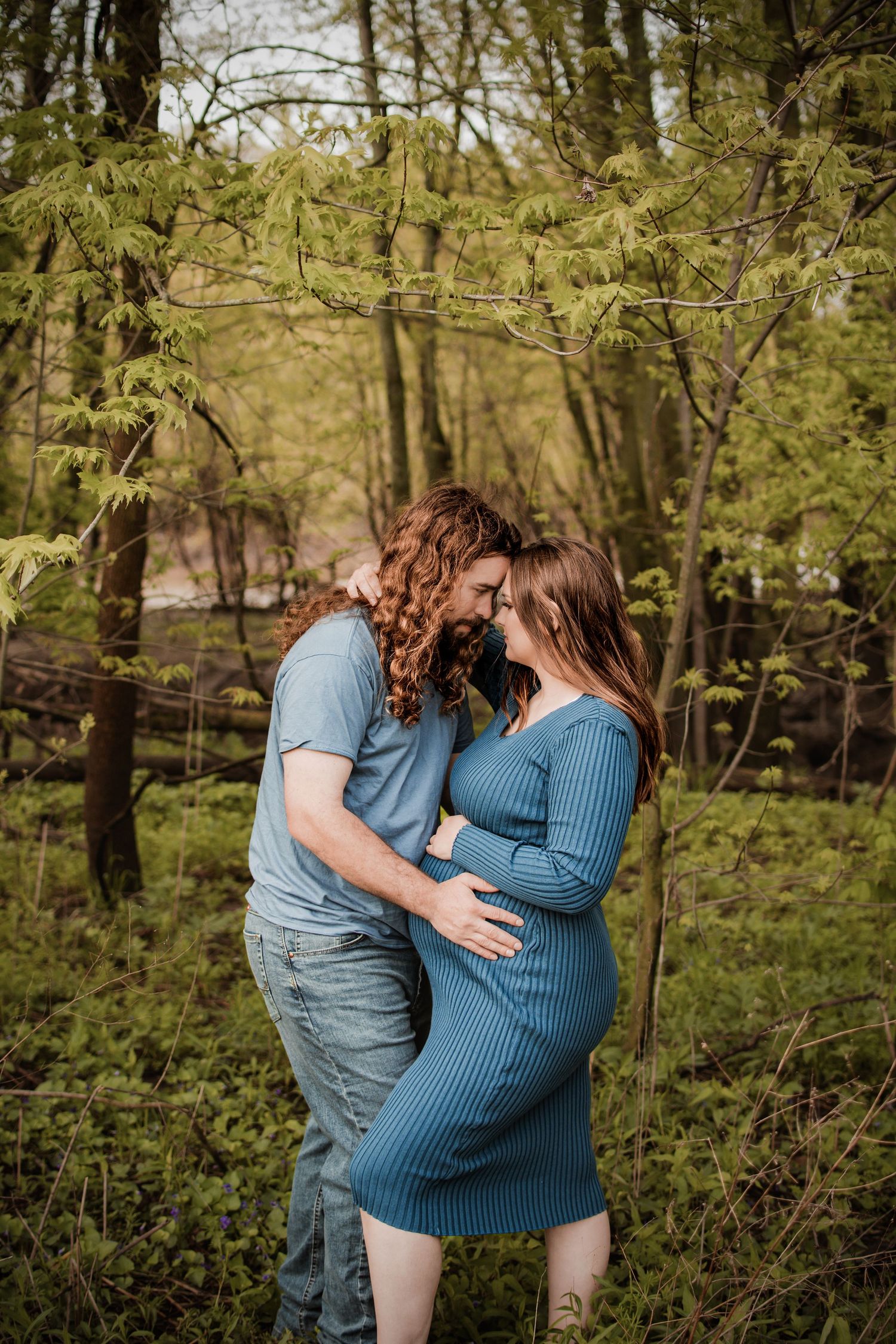 Romantic embrace in a wooded setting with spring foliage.