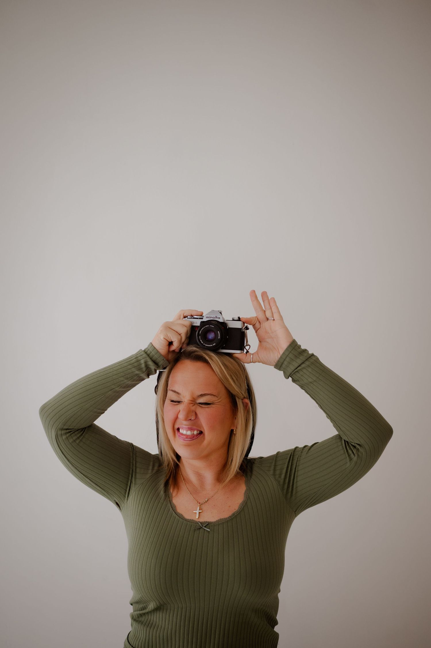 Person in olive green sweater takes selfies with vintage camera against neutral background in sequence of poses.