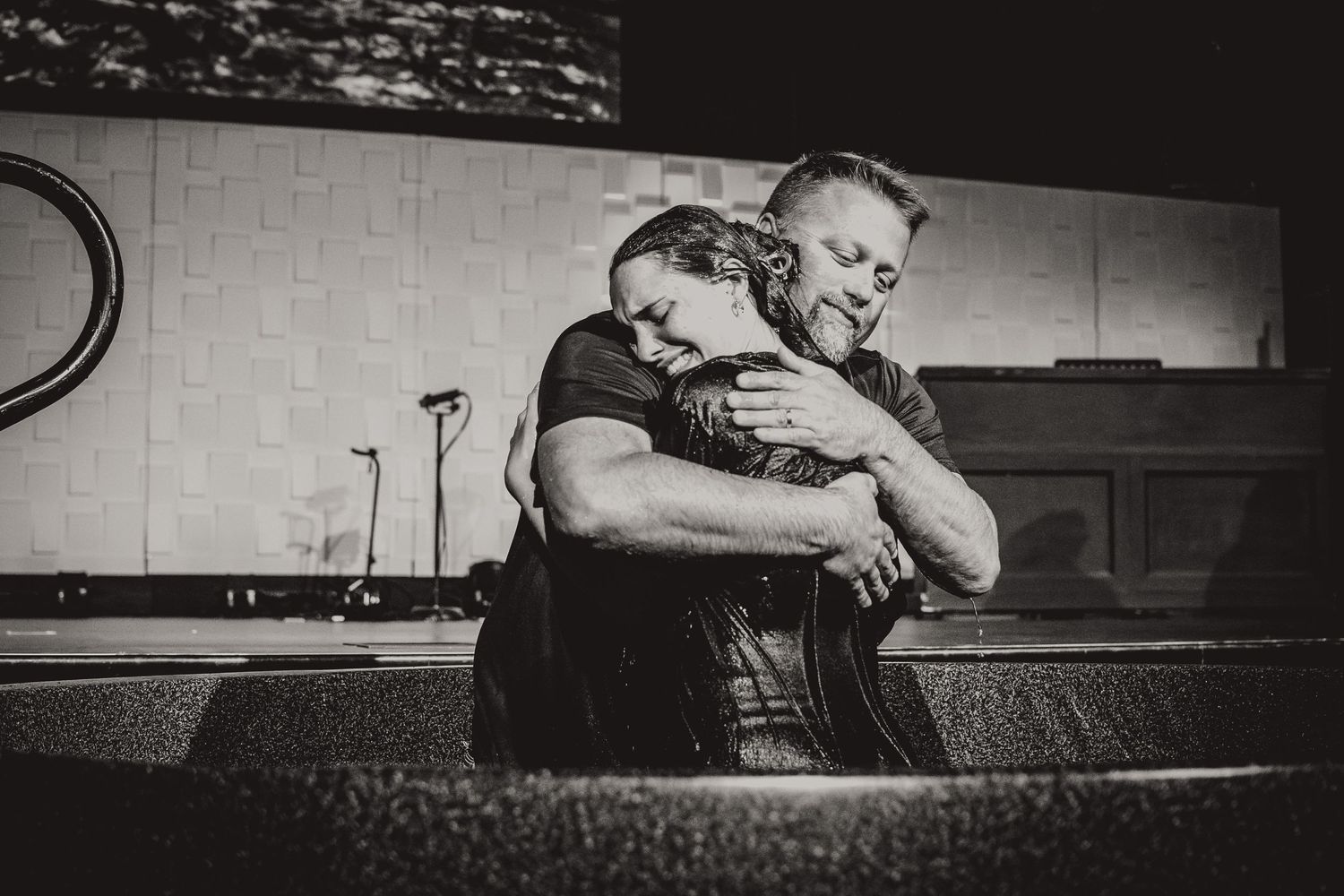 A black and white photograph showing a tender embrace at a church baptismal pool.