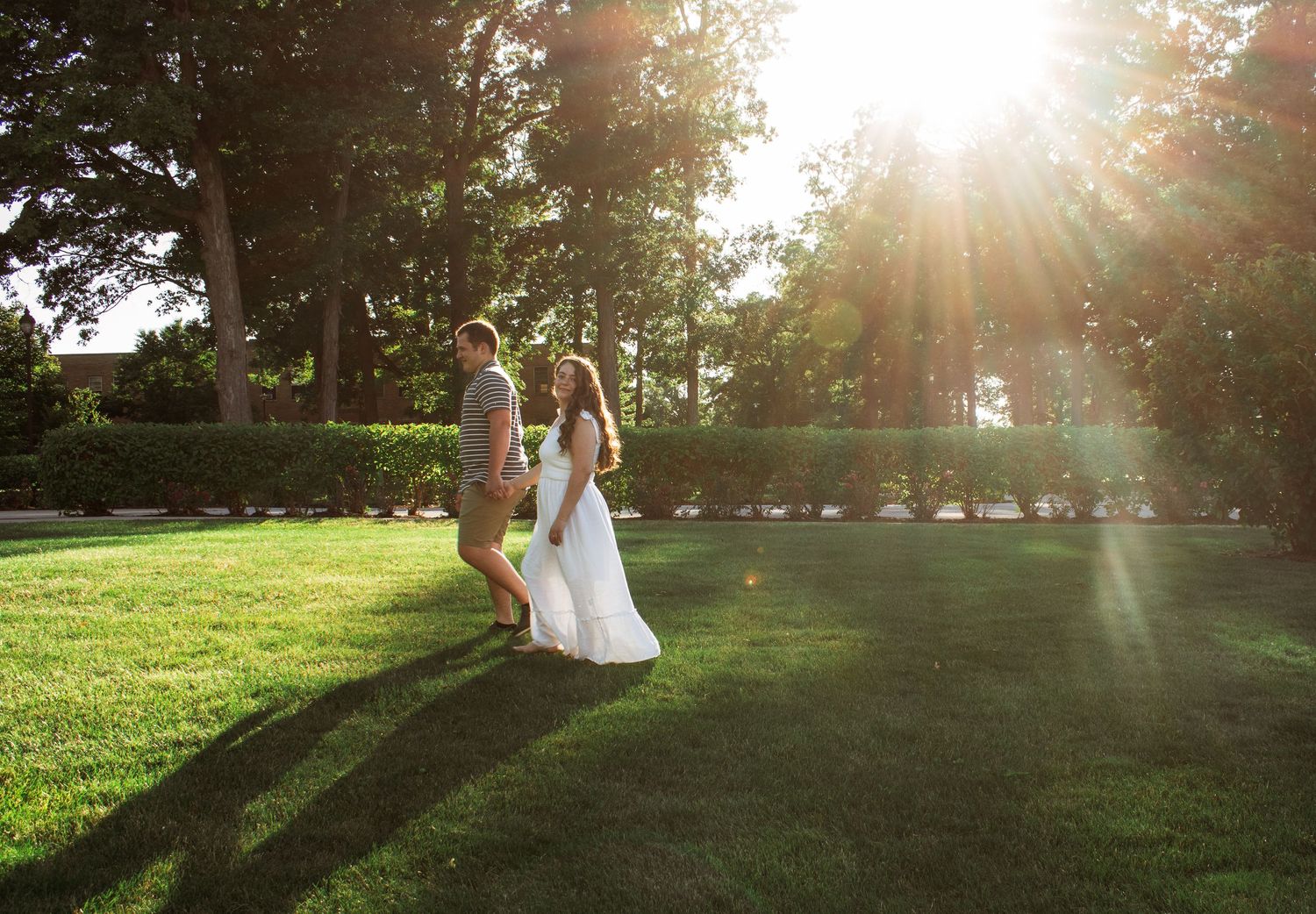 Couple walking on a sunlit lawn with beautiful lens flare and trees in the background.
