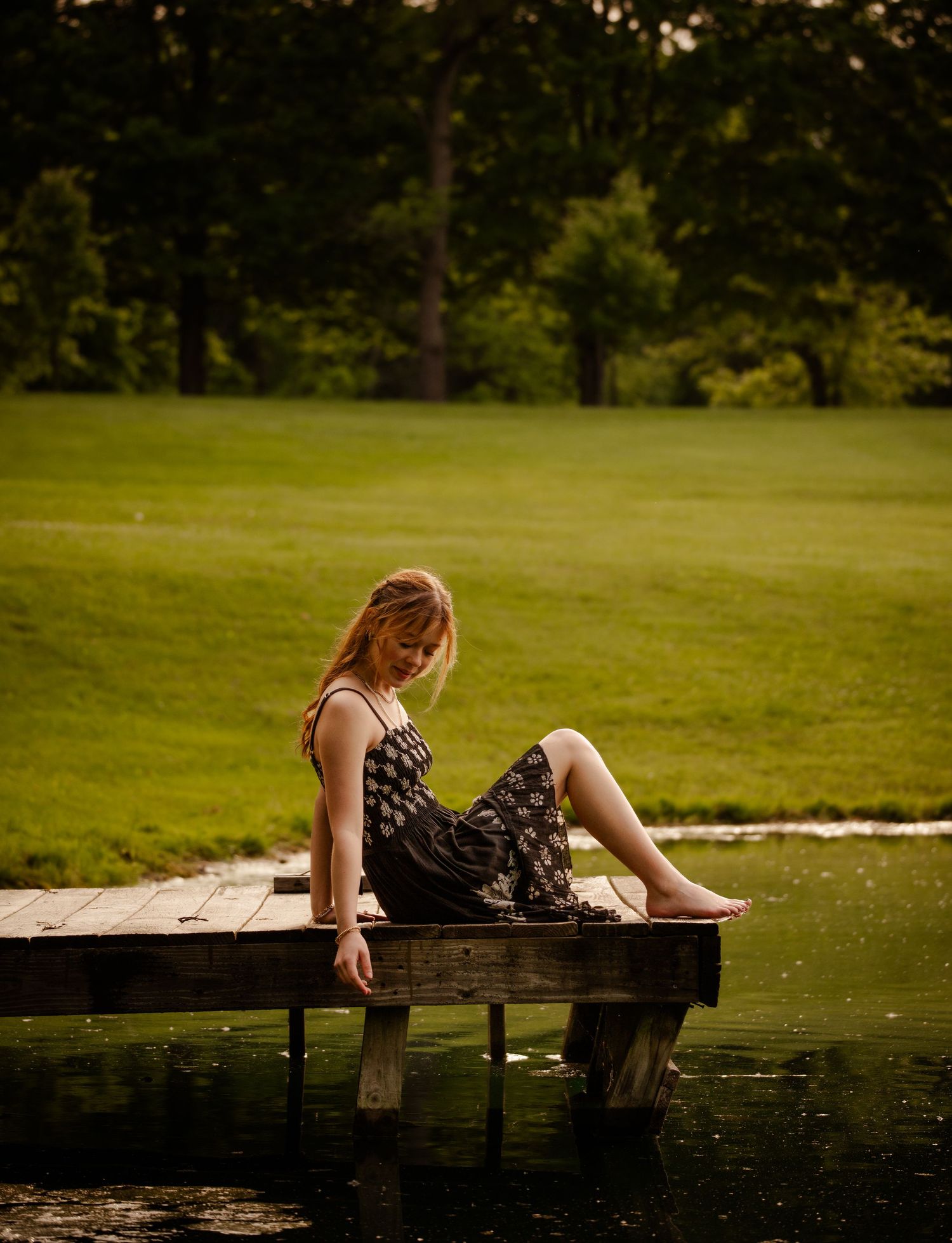 An elegant sundress-clad figure lounges peacefully on a wooden dock by a serene lake during golden hour.