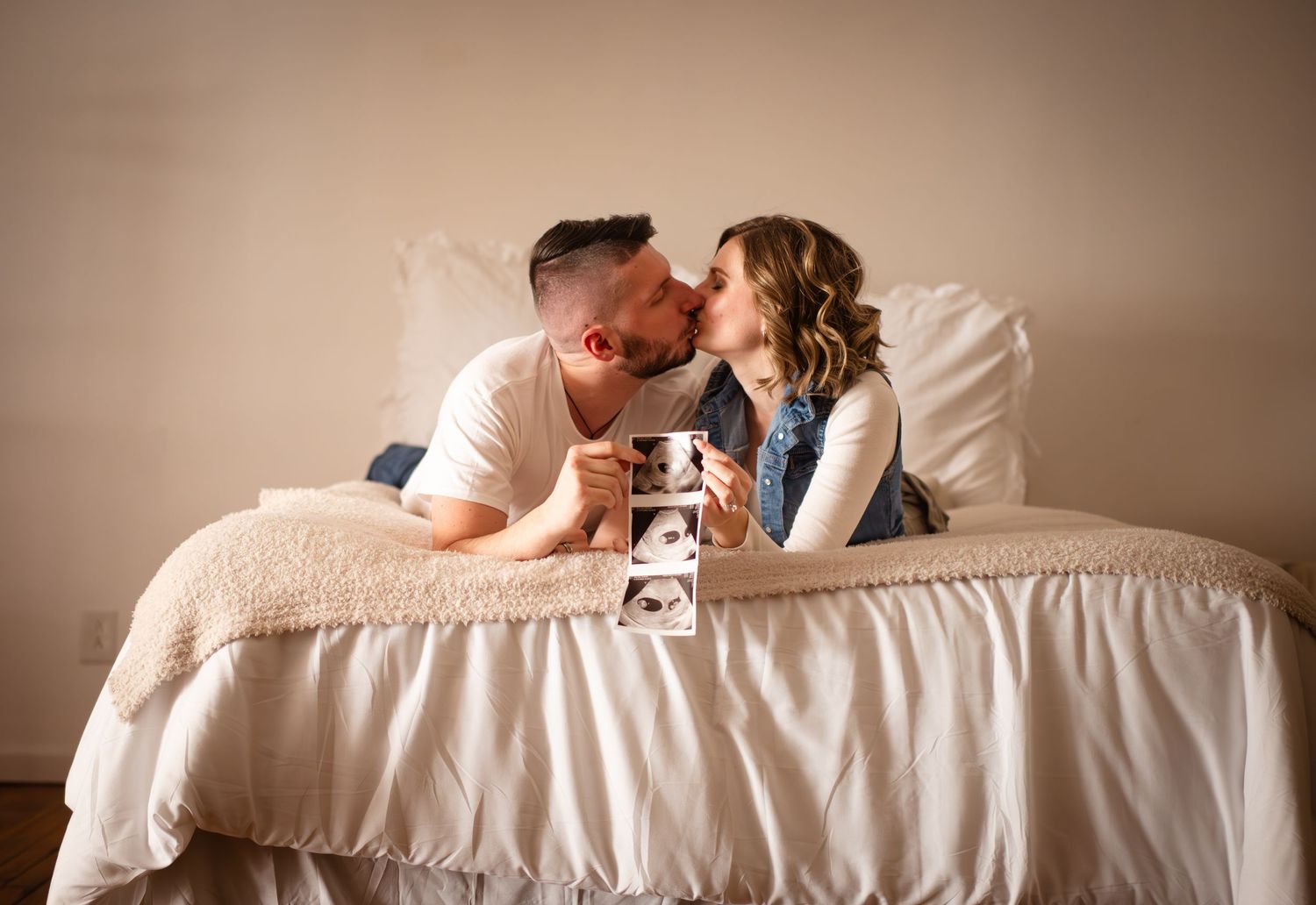 Couple sharing an intimate moment on bed while holding ultrasound photo.