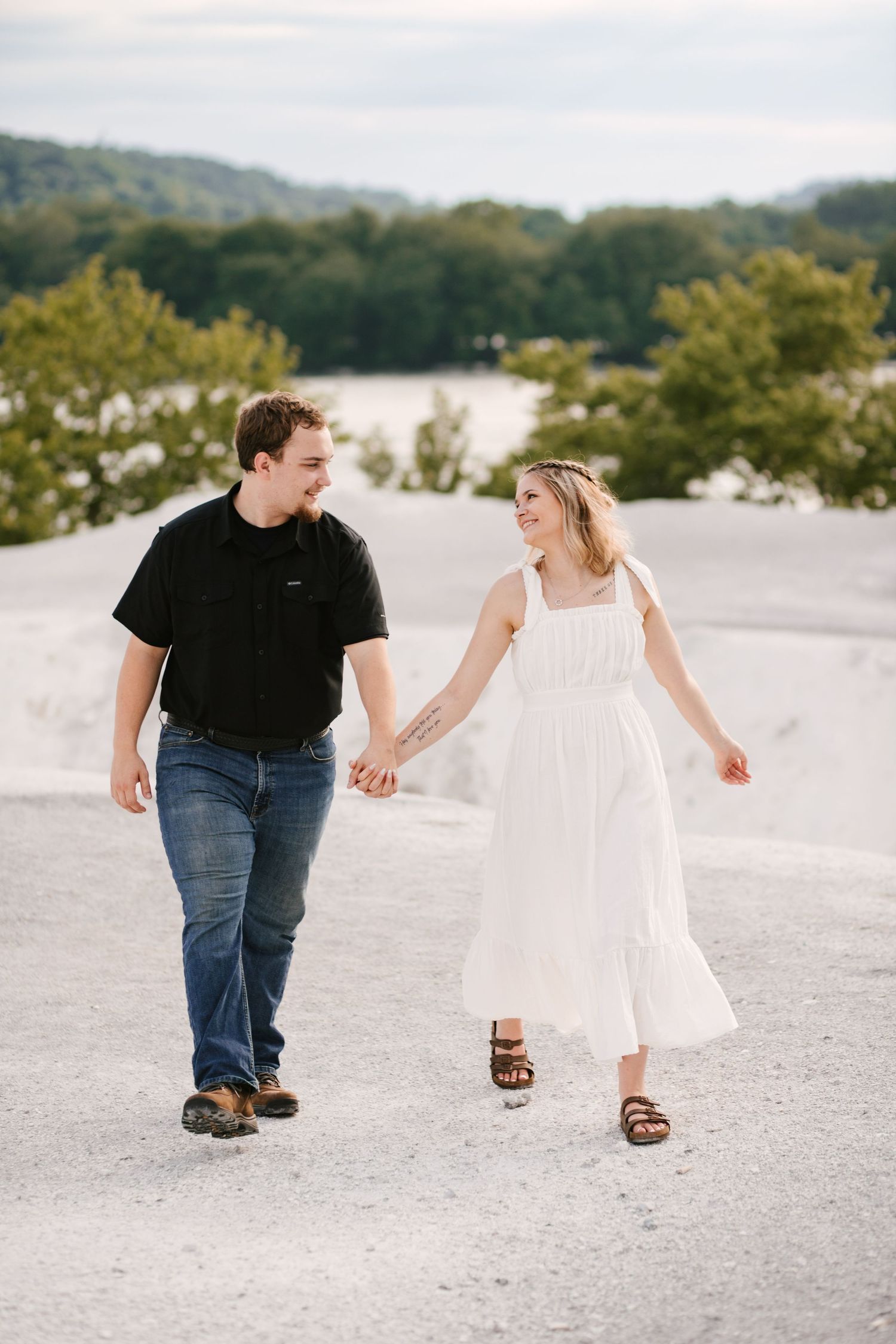 Playful couple walking and laughing together on a white sandy beach path.