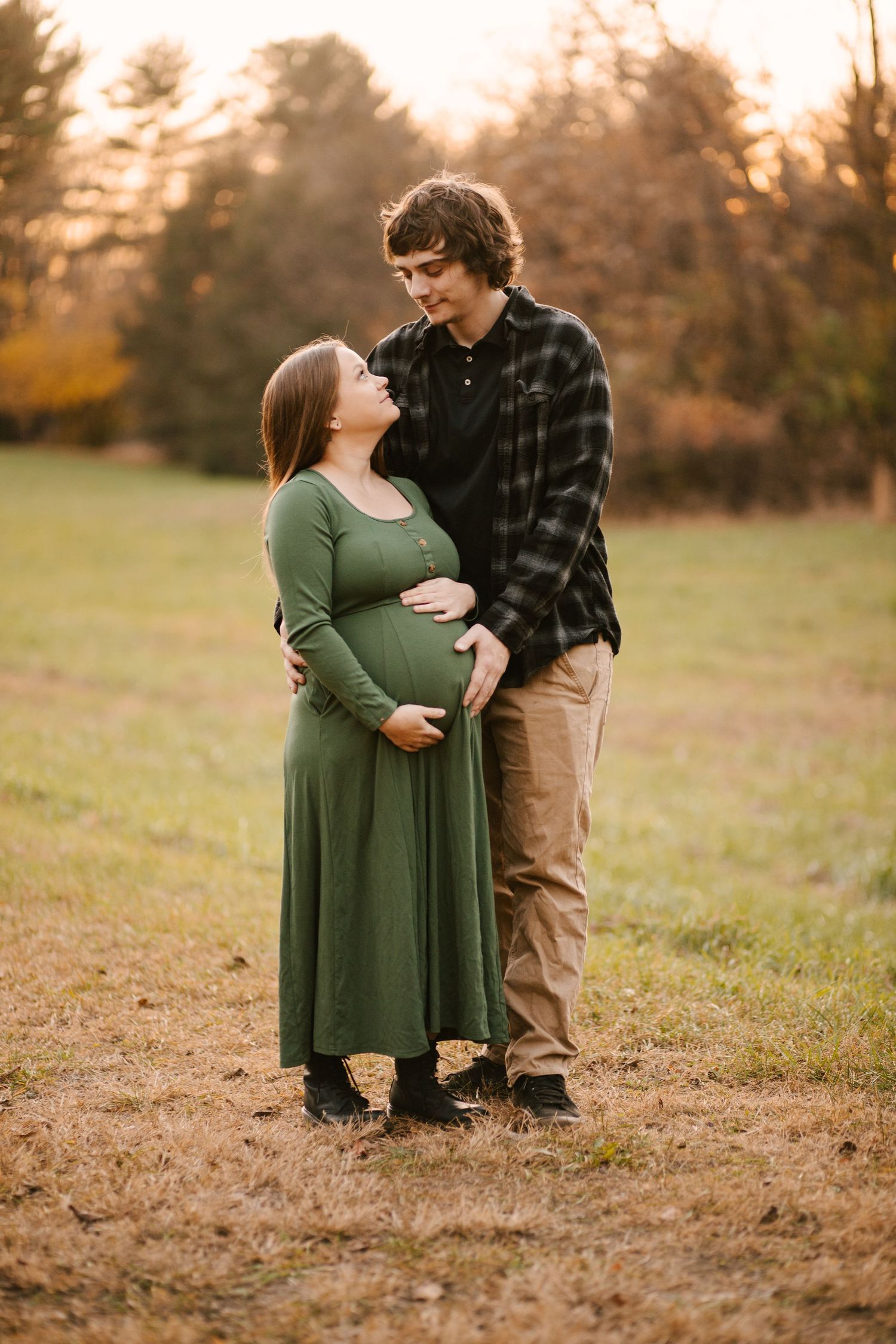 Couple poses lovingly in a field during autumn sunset.