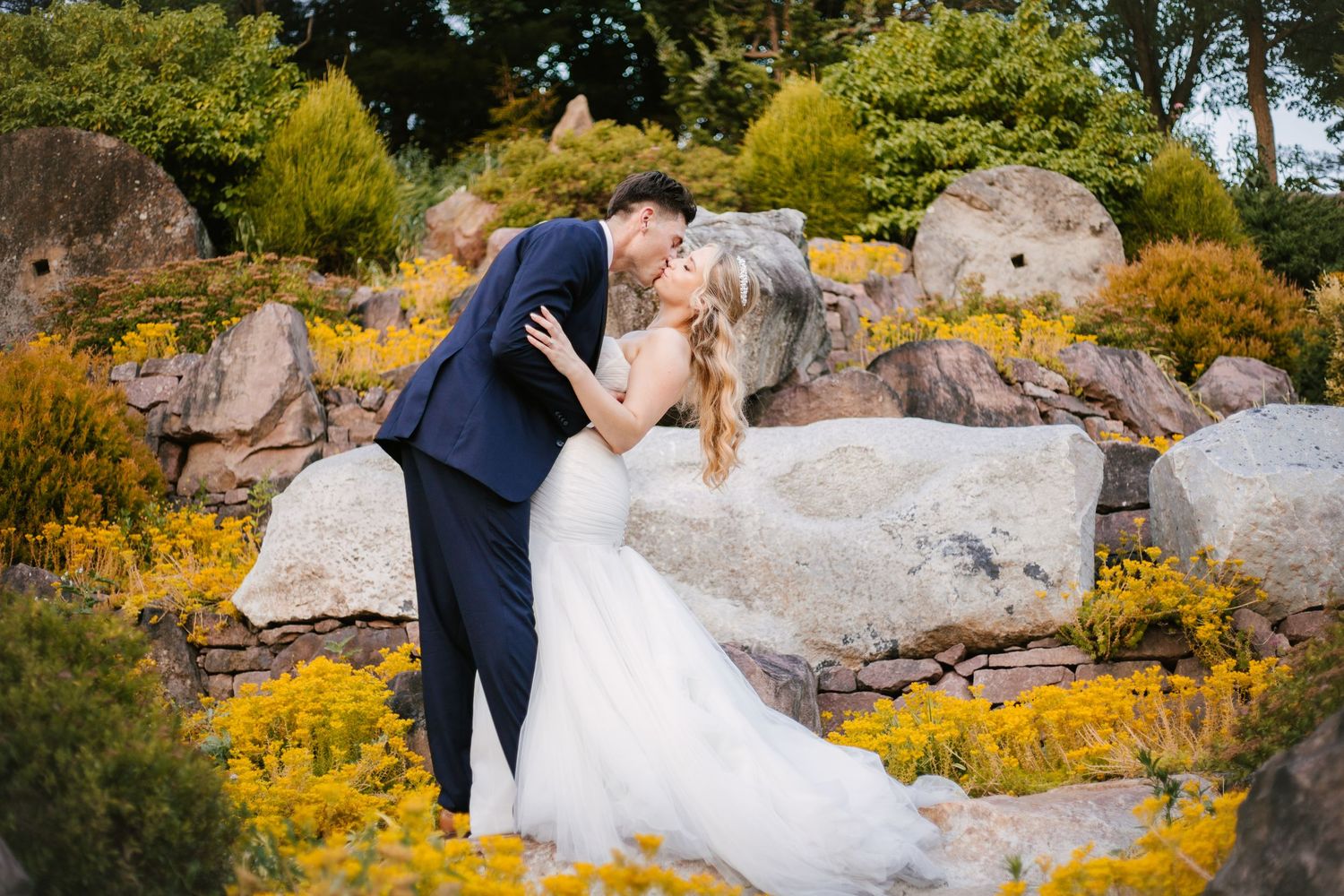 Wedding couple poses among yellow autumn flowers and natural rock formations.