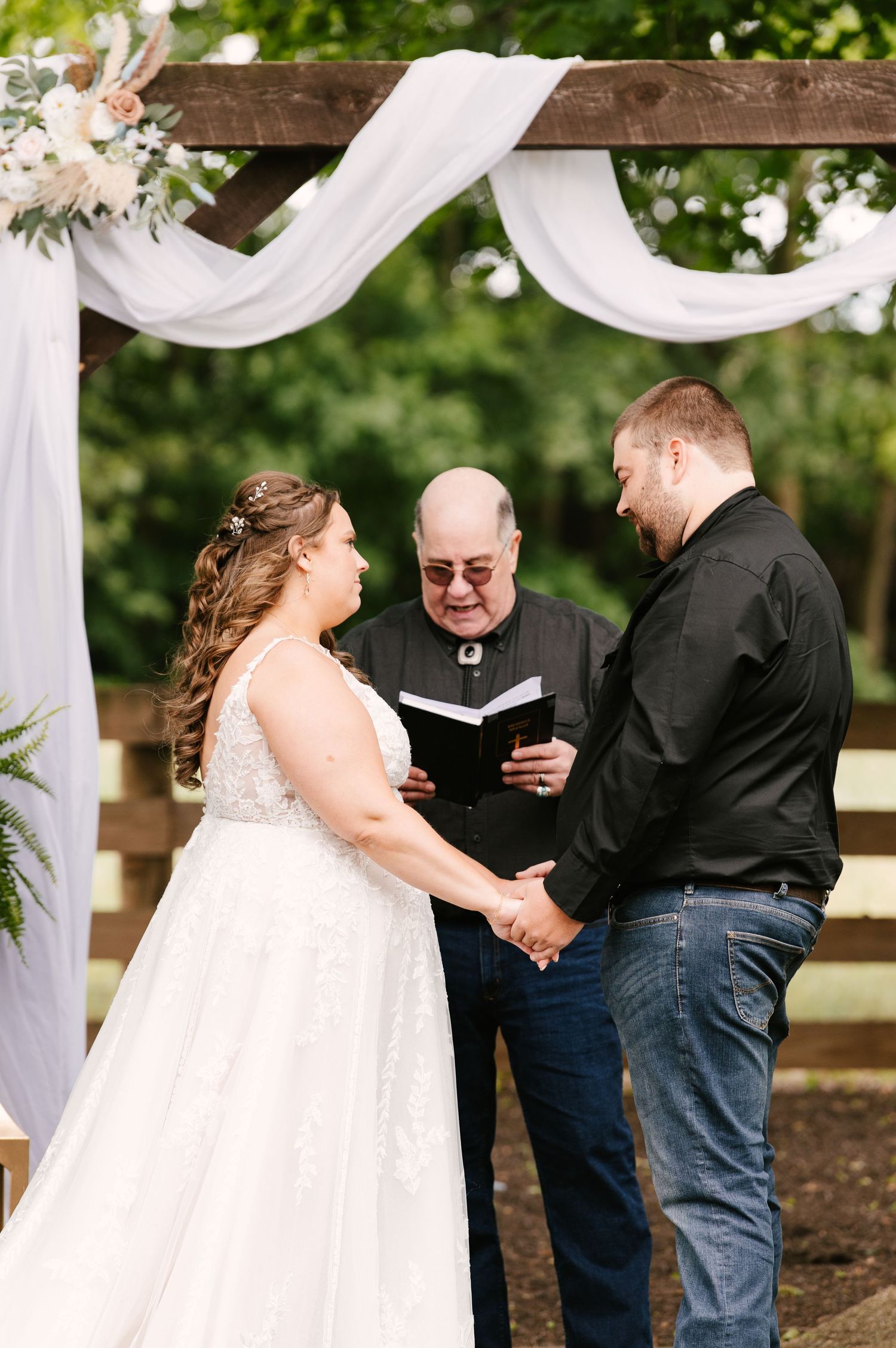 Outdoor wedding ceremony under white draped arch with natural greenery.