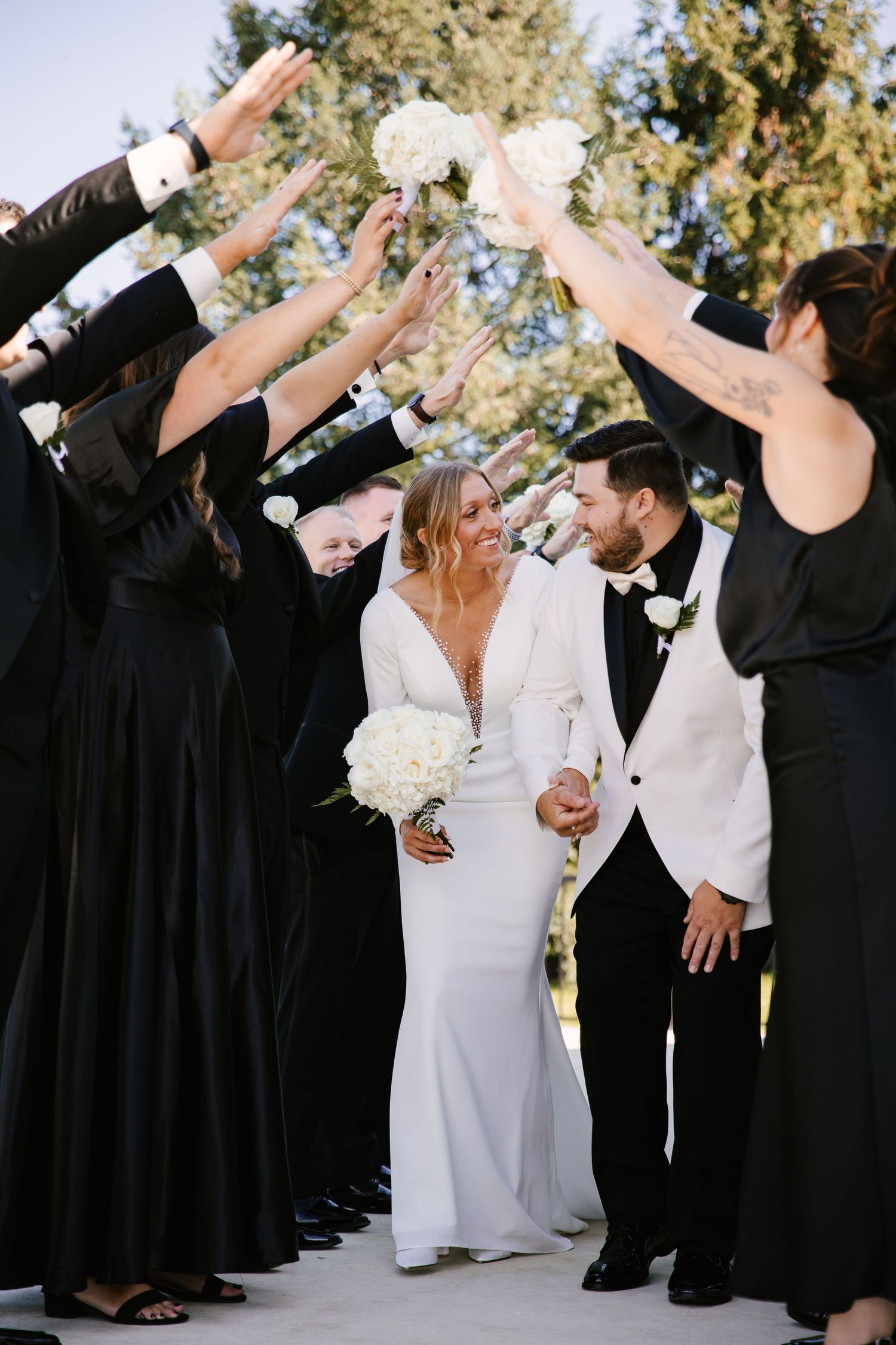 Wedding party forms a celebratory arch tunnel with raised arms as couple walks through in formal attire.