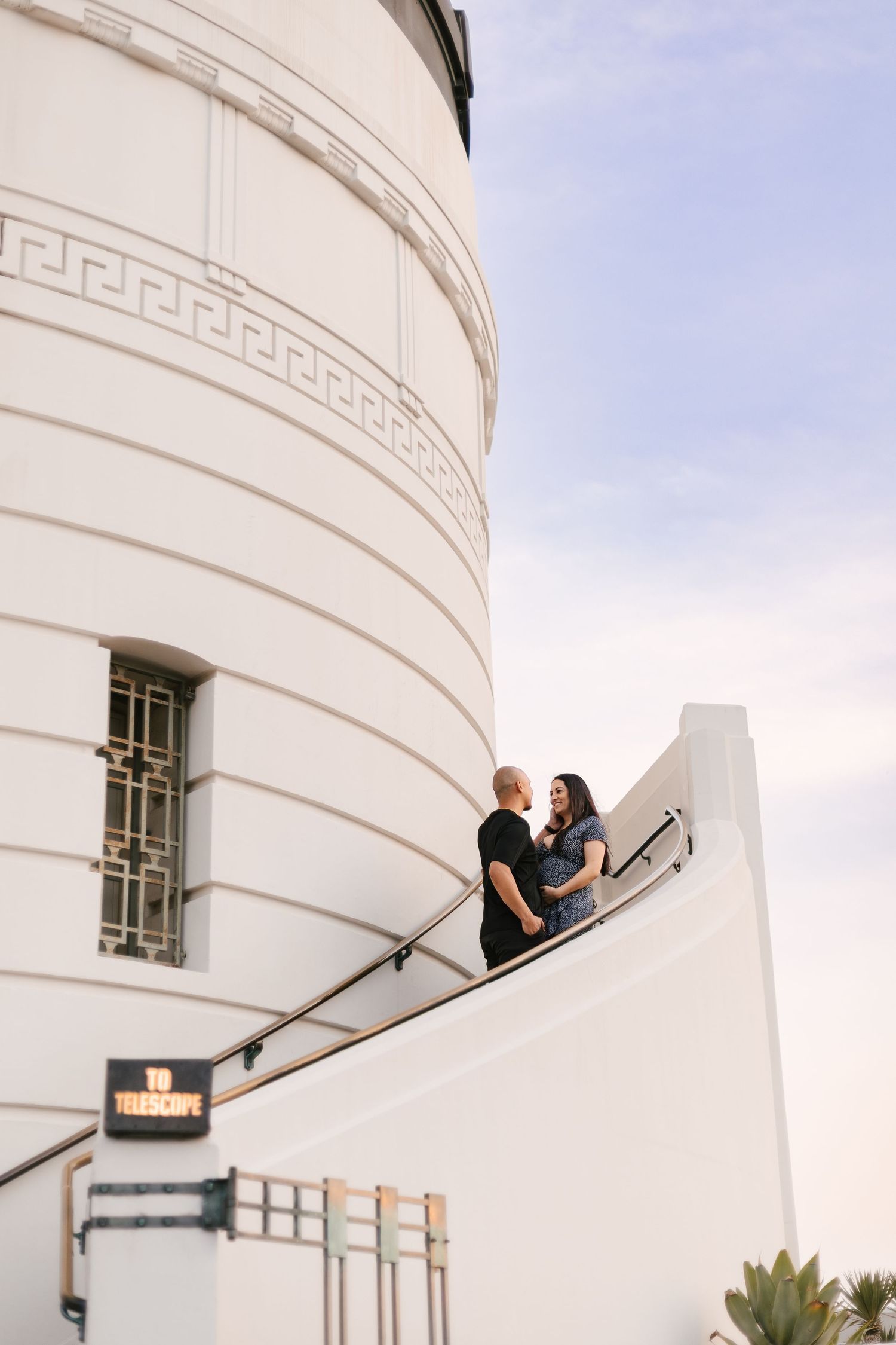 Couple shares a romantic moment against a white architectural backdrop during a photoshoot.