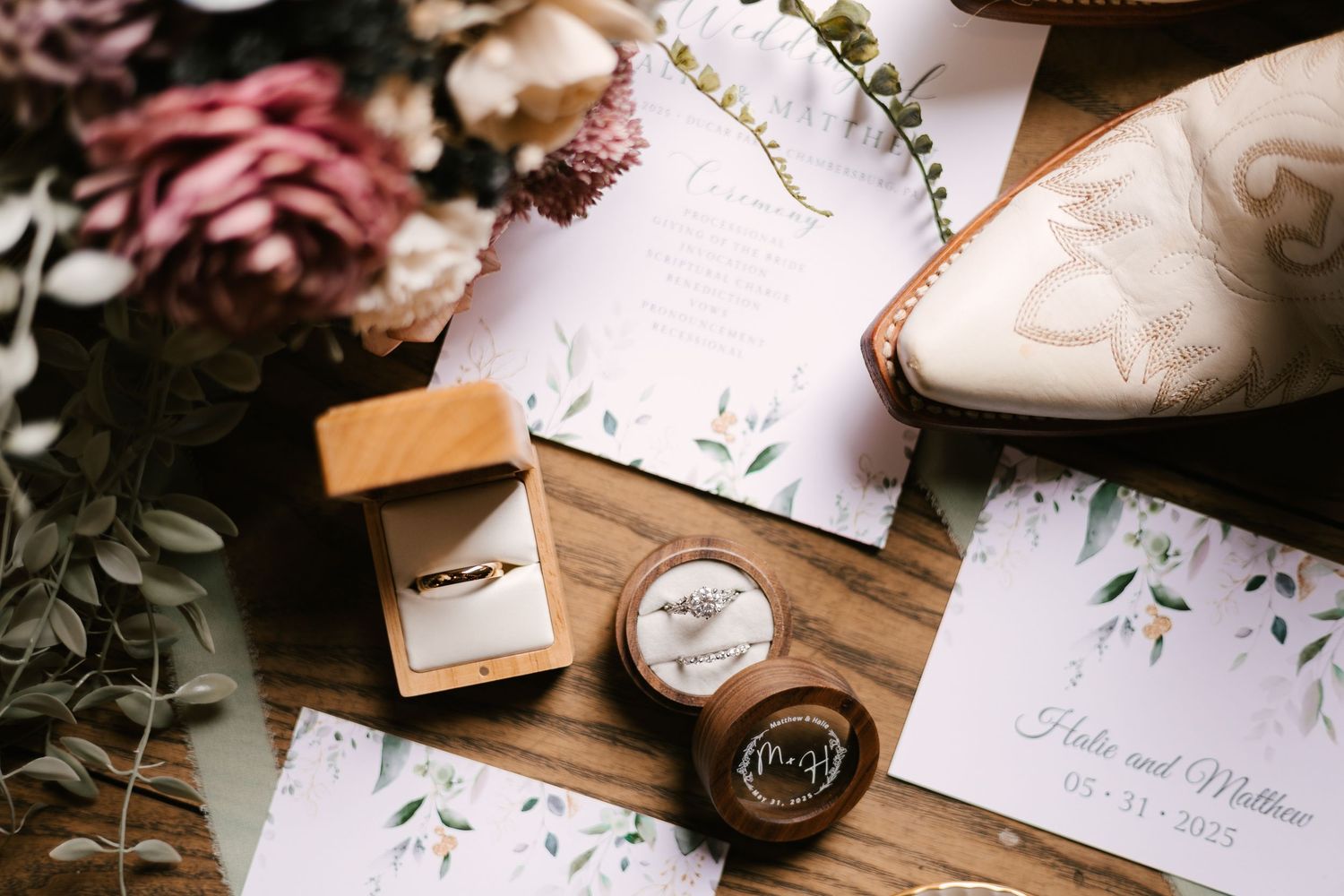 Wedding details including invitations, rings, and floral elements arranged on wooden surface.