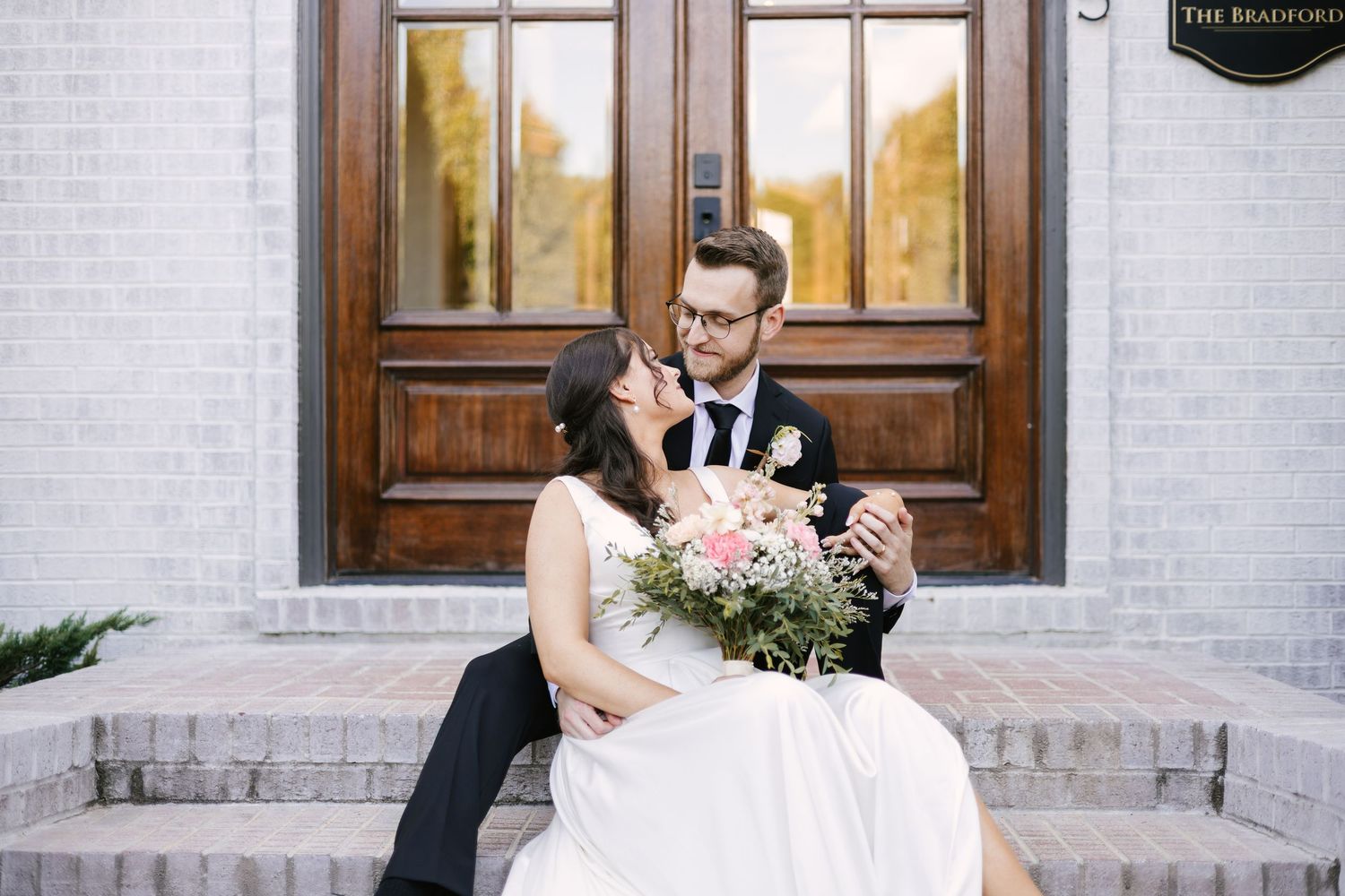 Wedding couple posing in front of a white brick building with wooden doors and steps.