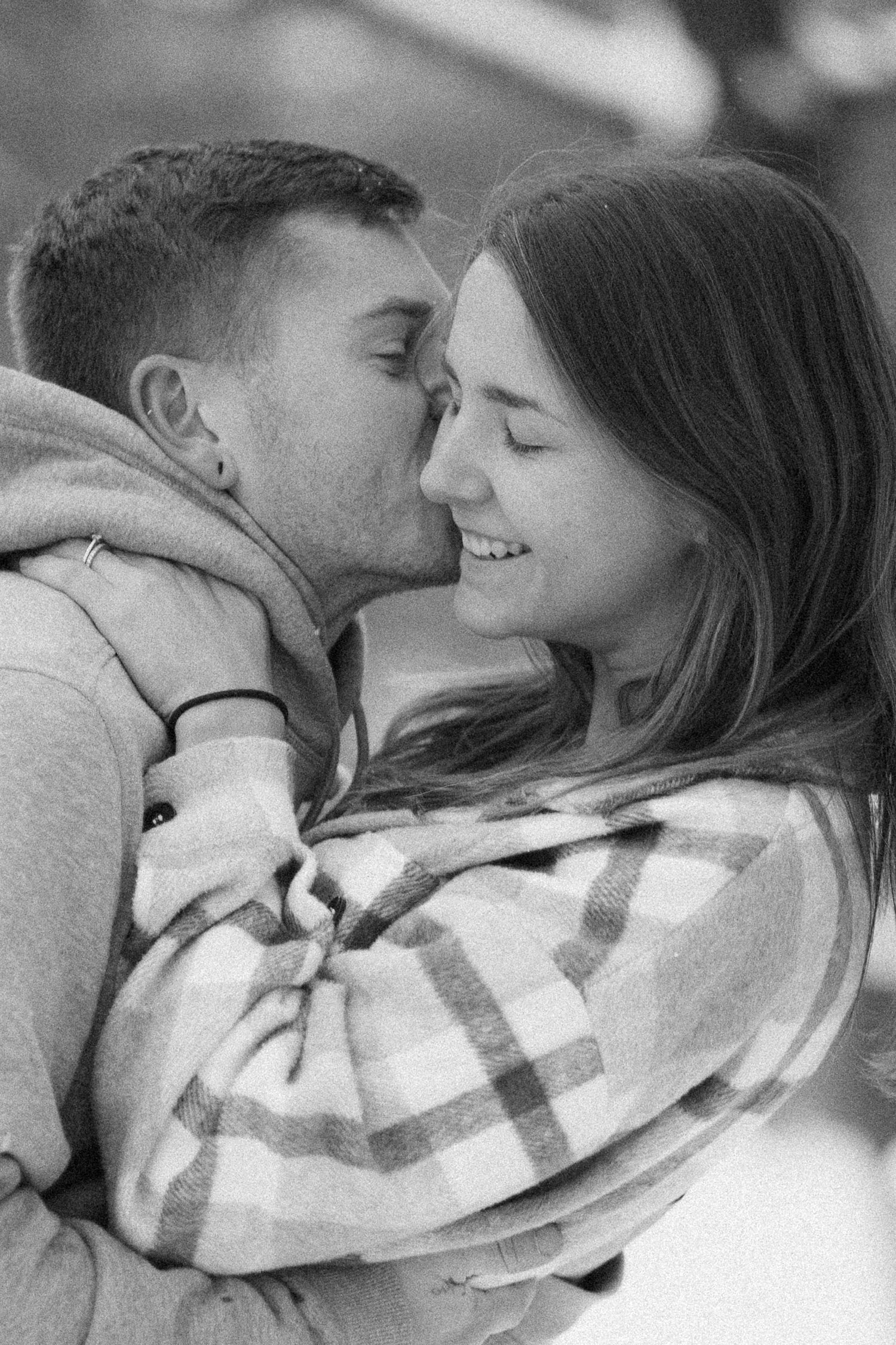 A cozy winter photoshoot featuring a couple wrapped in a plaid blanket.