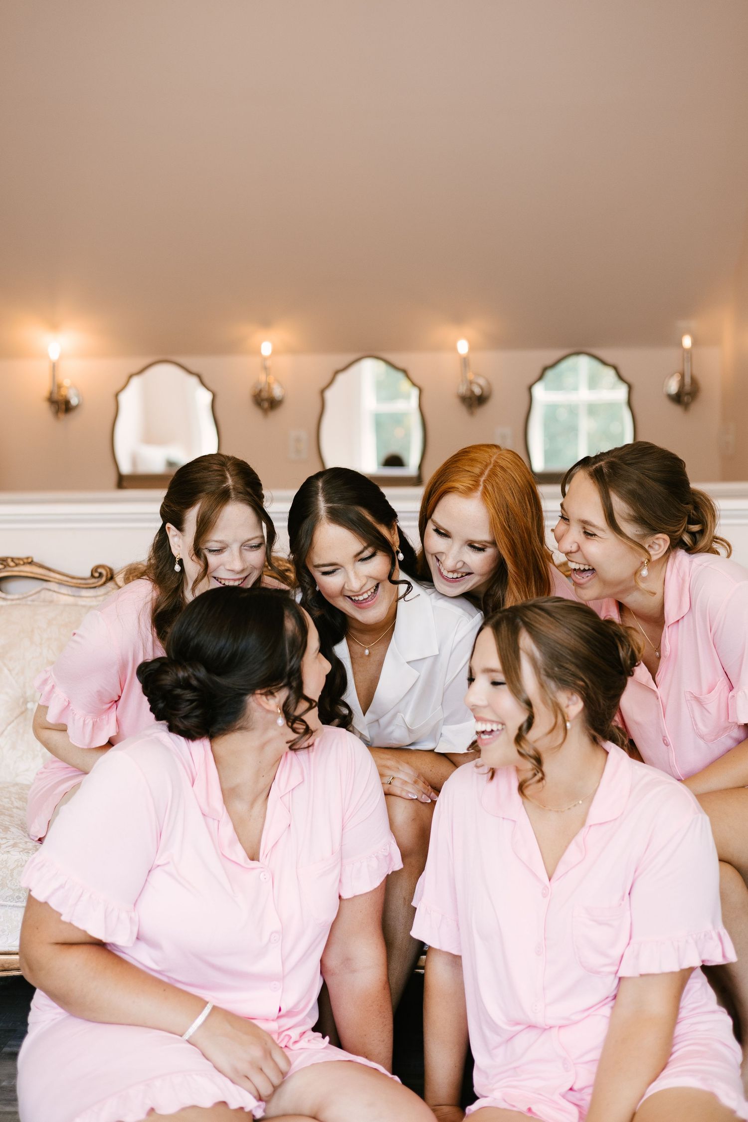 Bridal party in matching pink robes sharing laughter during wedding preparations.
