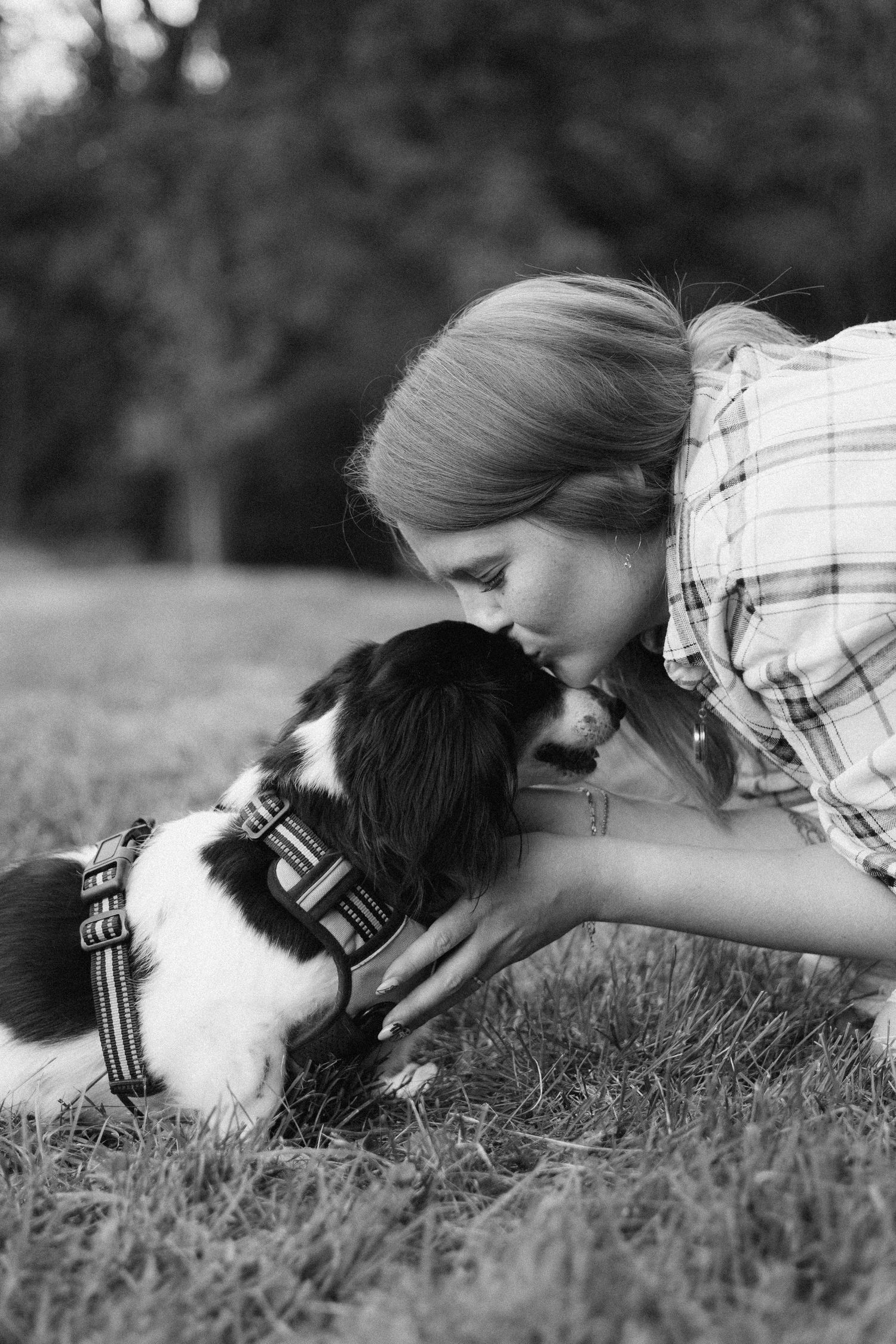 Black and white photo showing affectionate moment between person and dog on grass.
