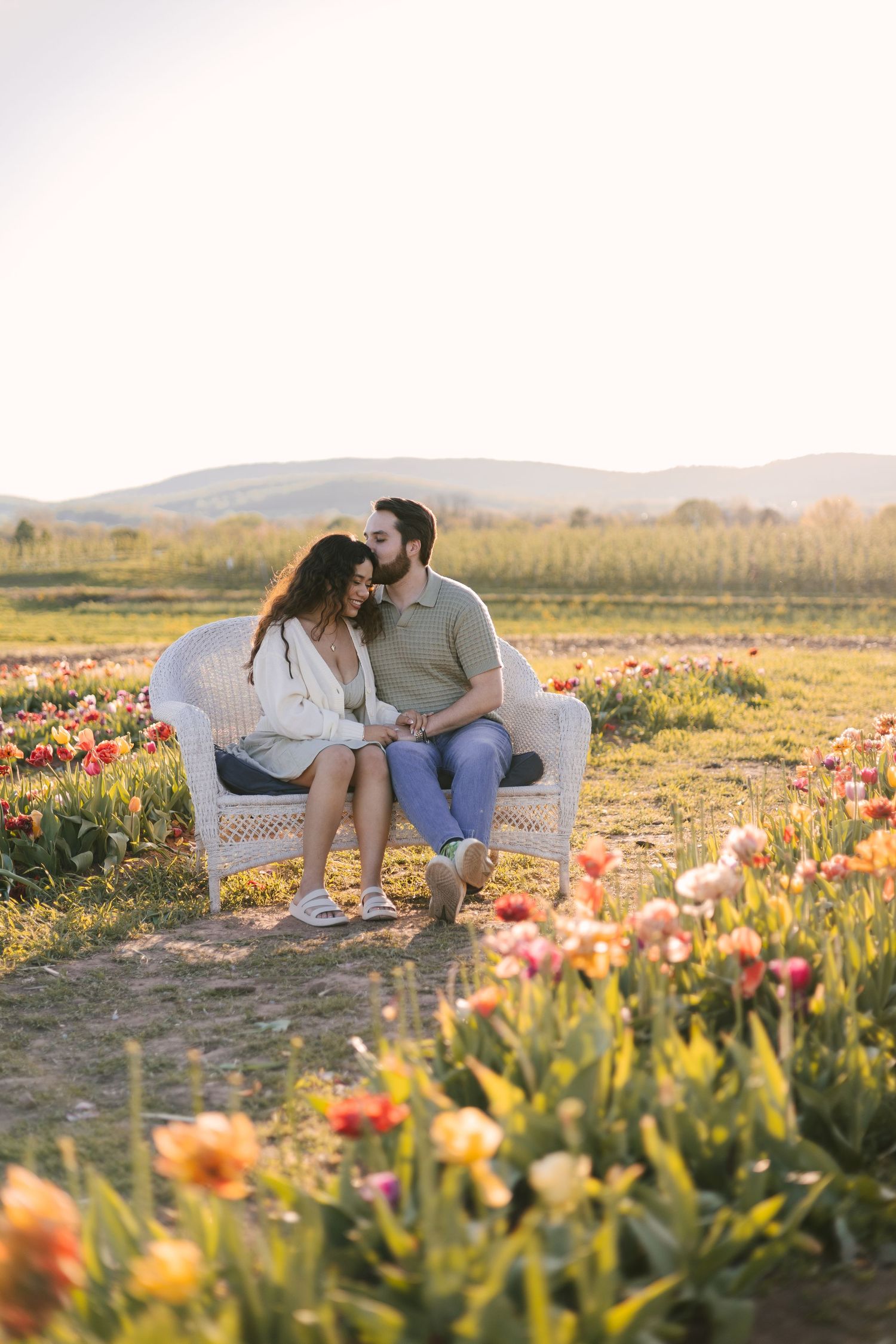 Couple relaxing on vintage white couch in blooming tulip field at golden hour.