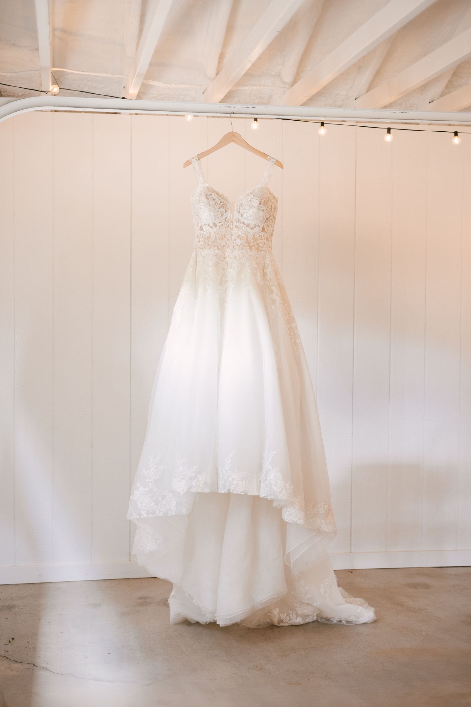 White wedding dresses hanging in a row against a bright white wall with exposed beams.