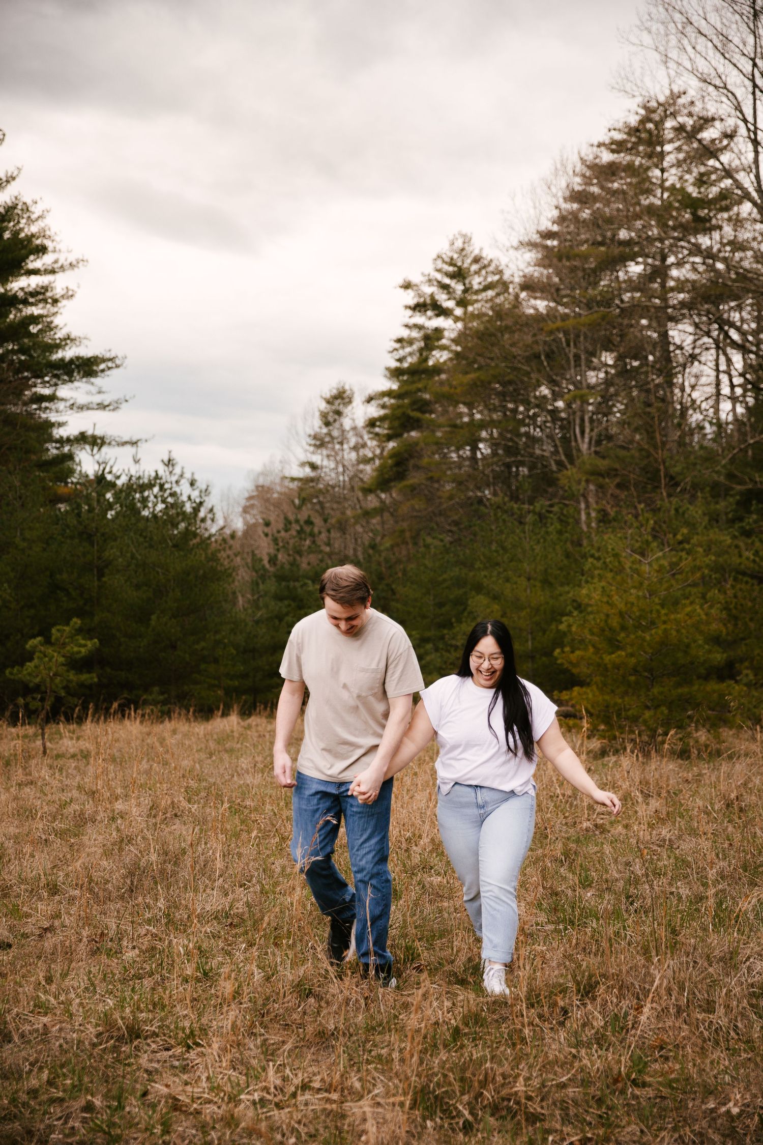 Couple walking through a rustic field with pine trees and mountains in the background.