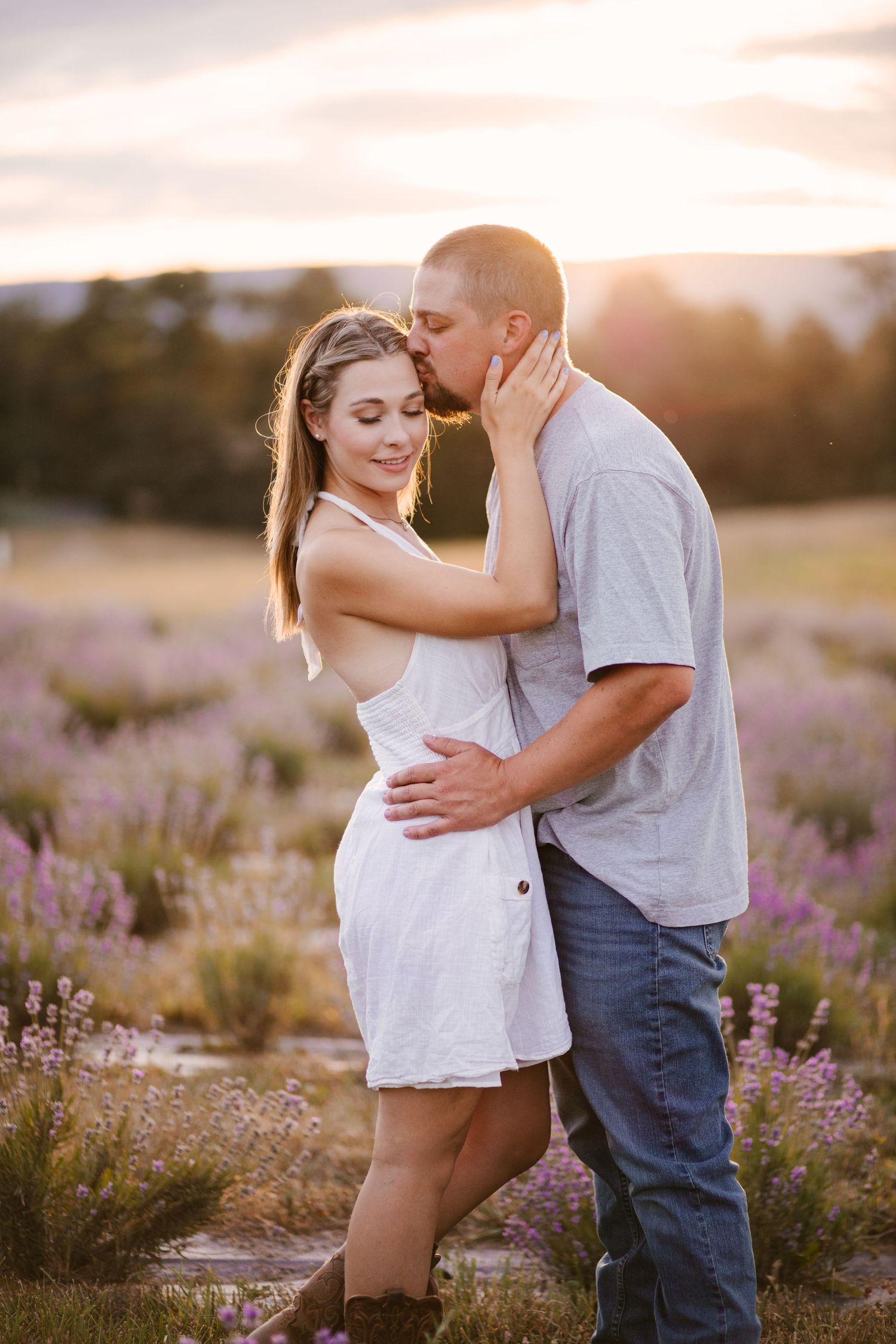 Romantic couple embracing in a field of purple wildflowers during golden hour sunset.