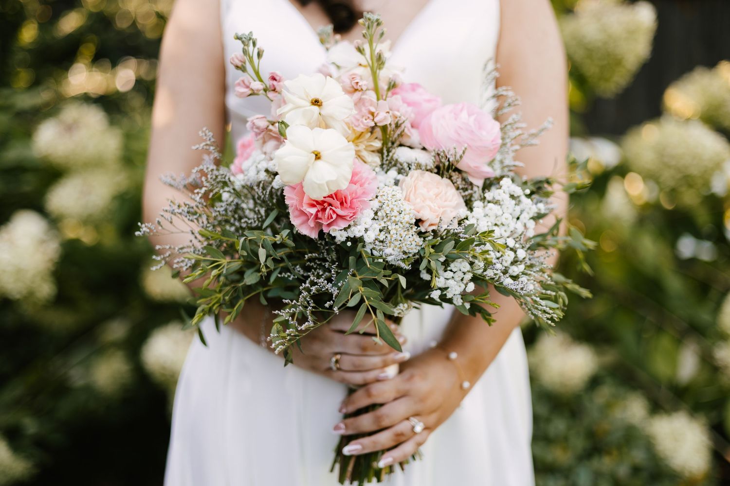 Elegant bridal bouquet with pink and white flowers held against a white wedding dress.