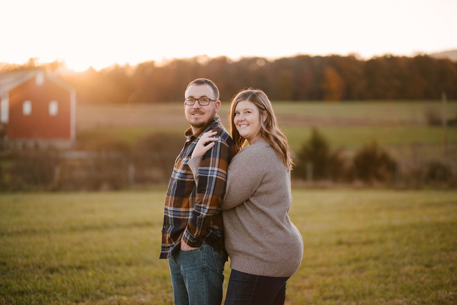 Couple embraces in casual sweaters during golden hour in an open field.