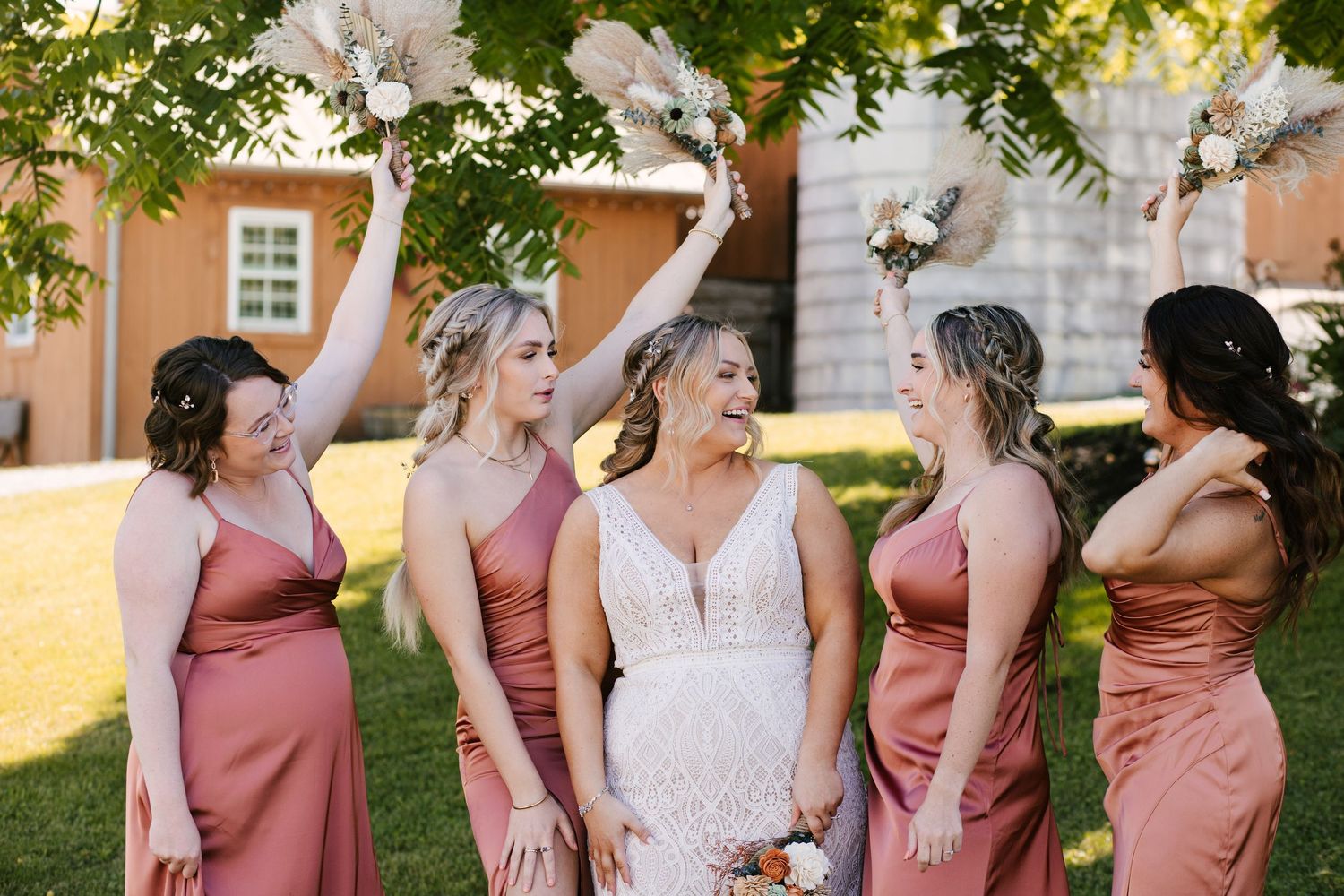 Bridesmaids in dusty rose dresses share a candid moment outdoors.