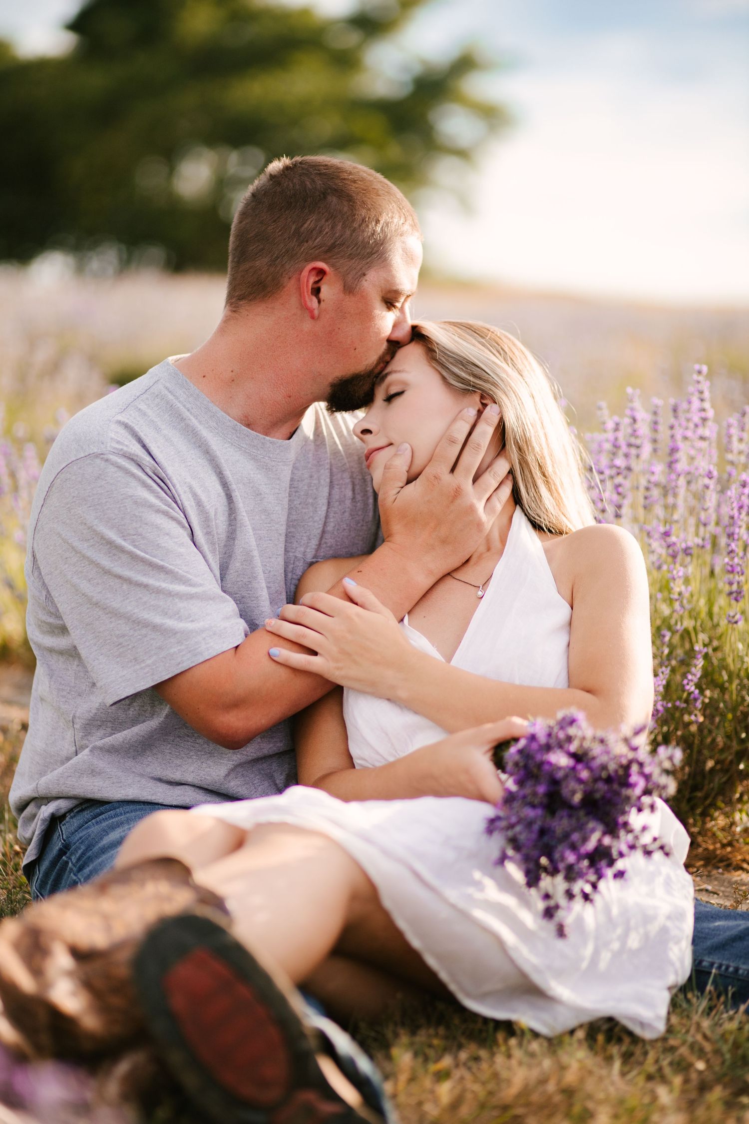 Couple shares romantic moment in field of purple wildflowers during sunset.