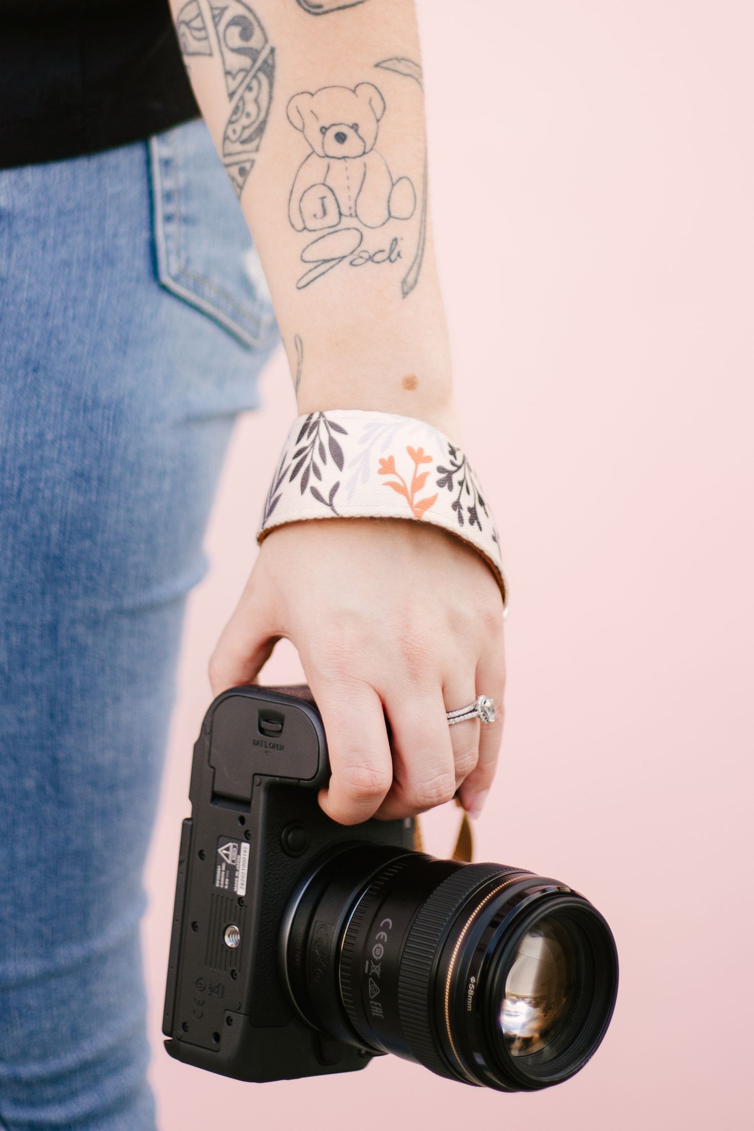 Close-up of tattooed hands holding professional camera equipment.