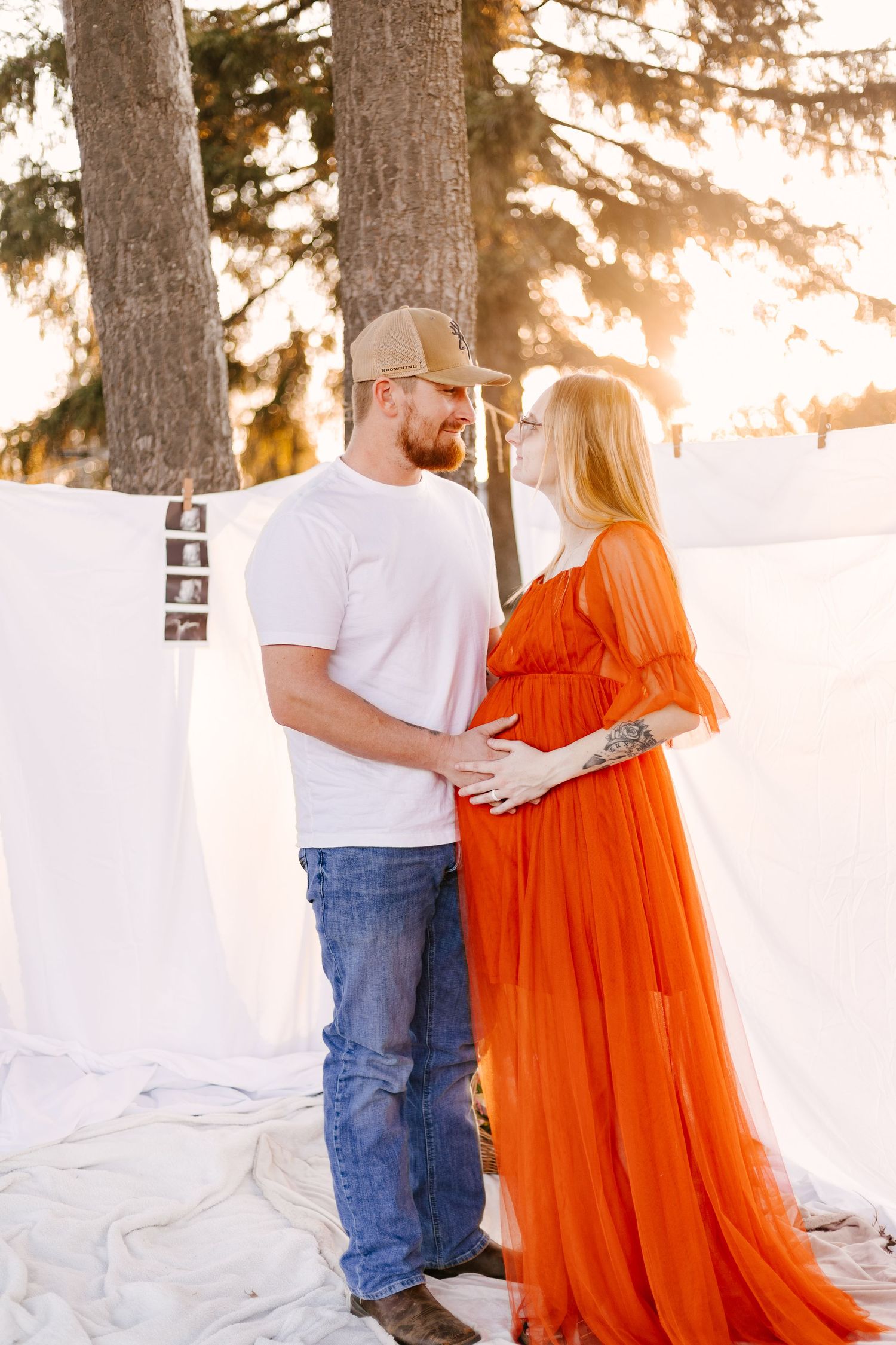 Couple in casual attire poses romantically against snowy white backdrop at golden hour.