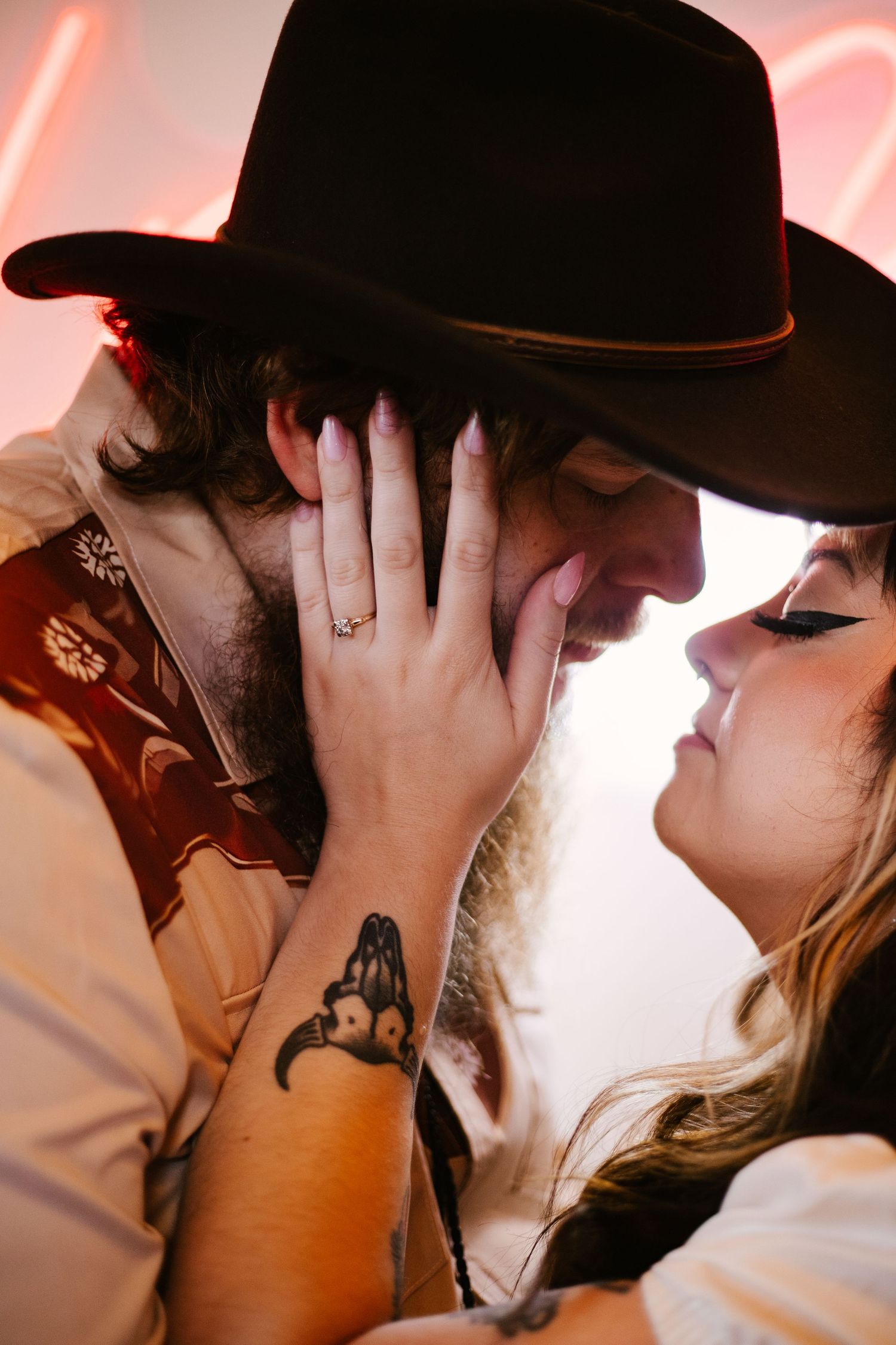 Couple in western attire shares intimate moment under red neon lighting.