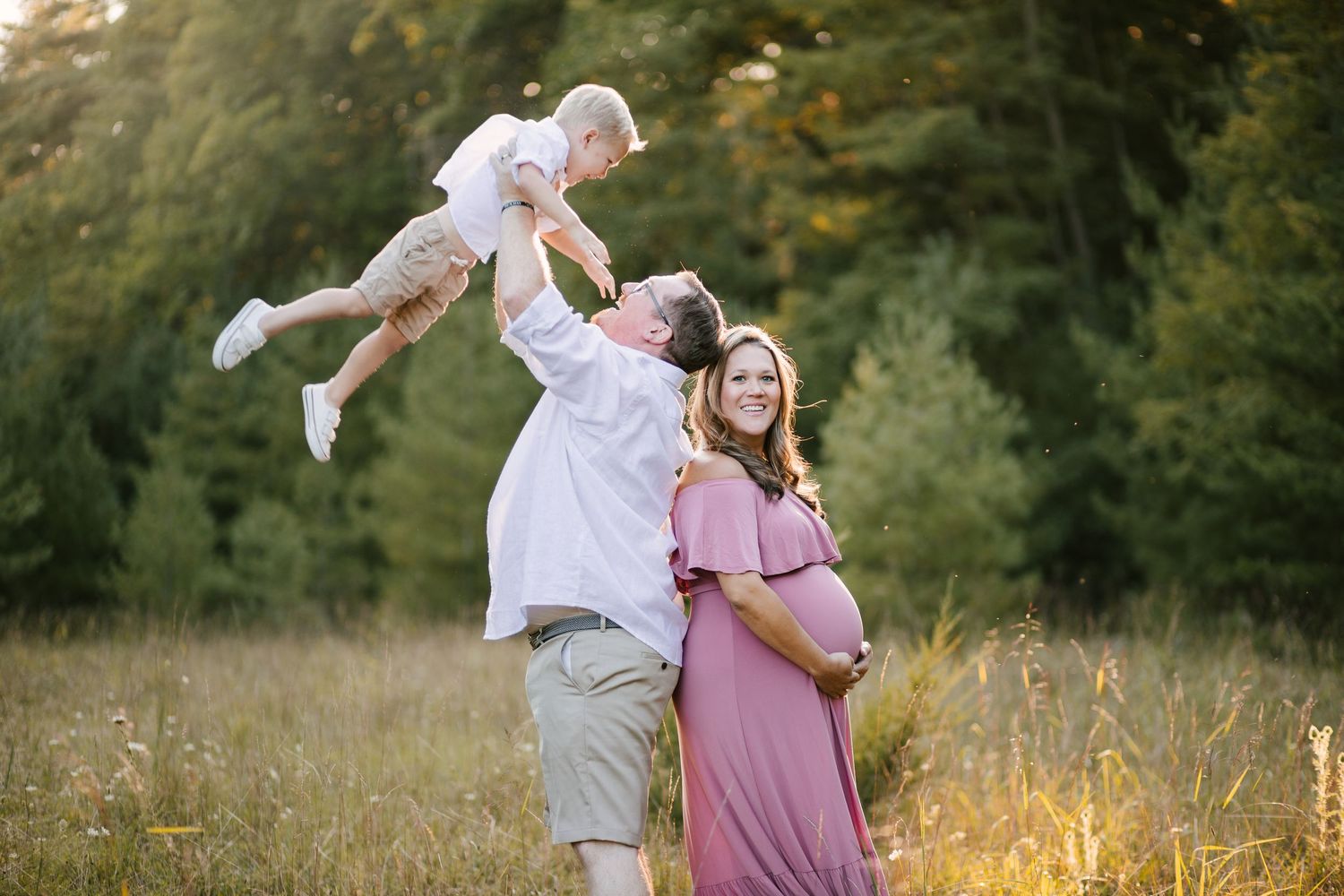 A joyful family moment during maternity photoshoot in a sunlit field.