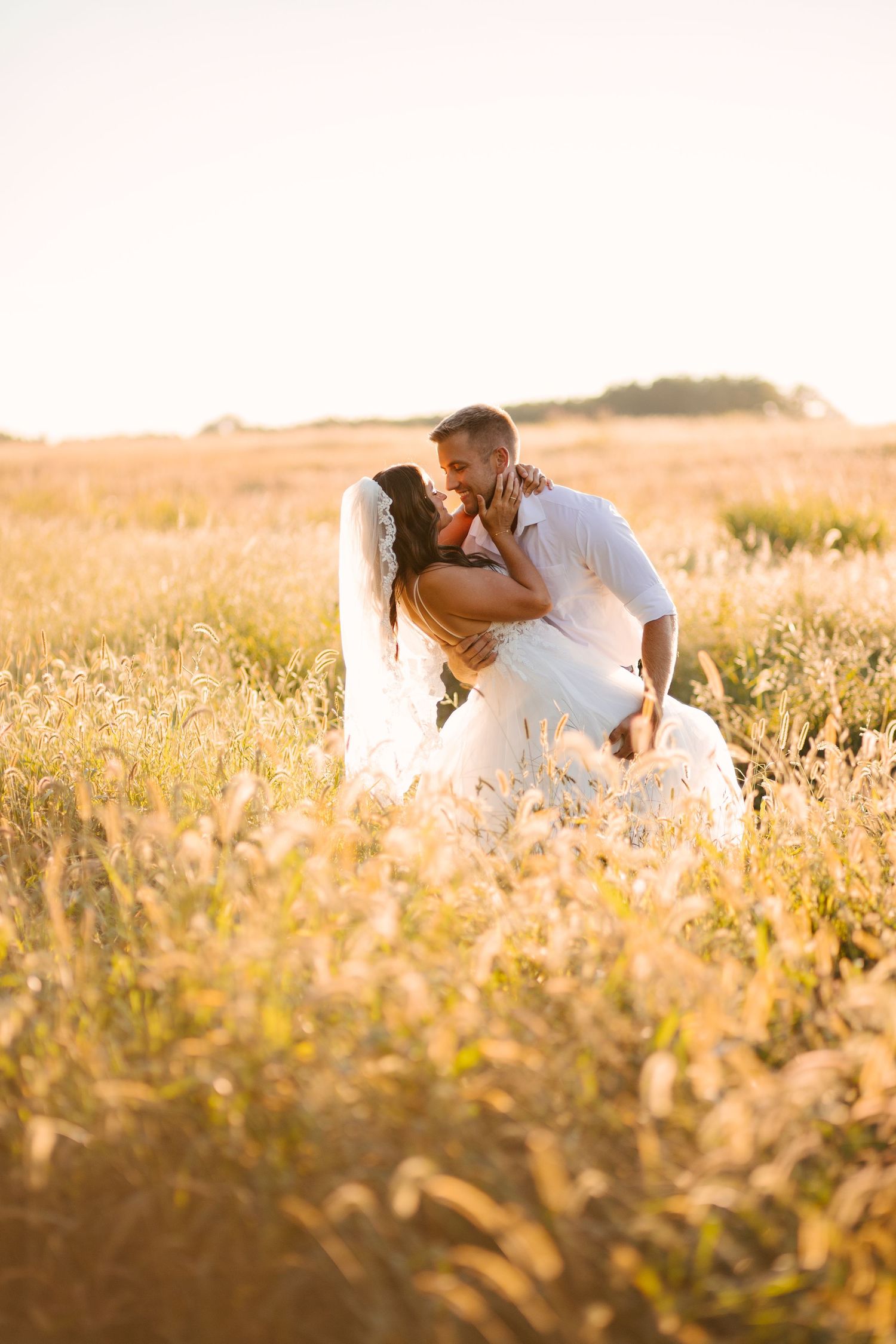 Romantic sunset photoshoot in a golden wheat field with soft glowing light.