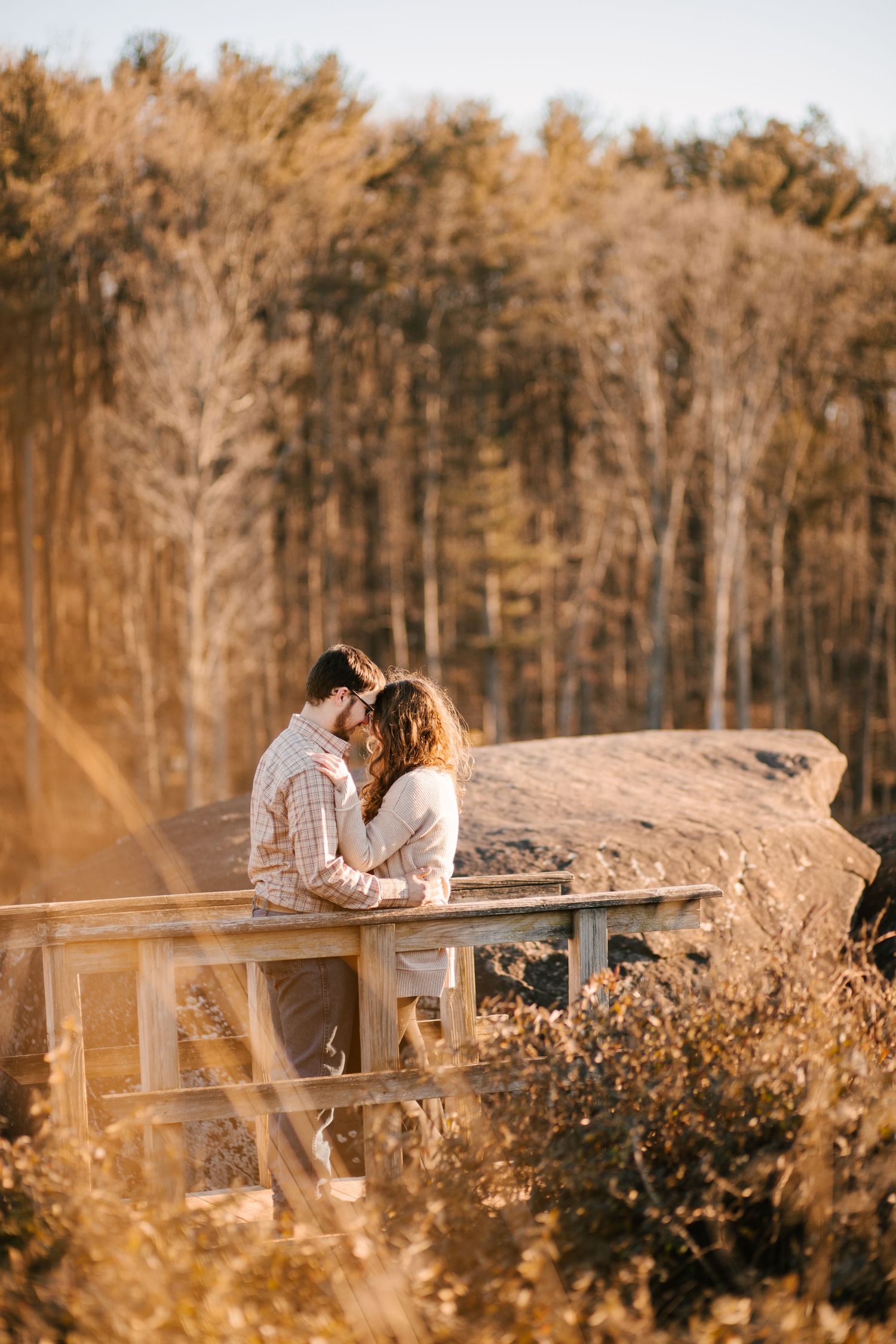 Couple shares intimate moment on wooden deck overlooking autumn forest landscape.