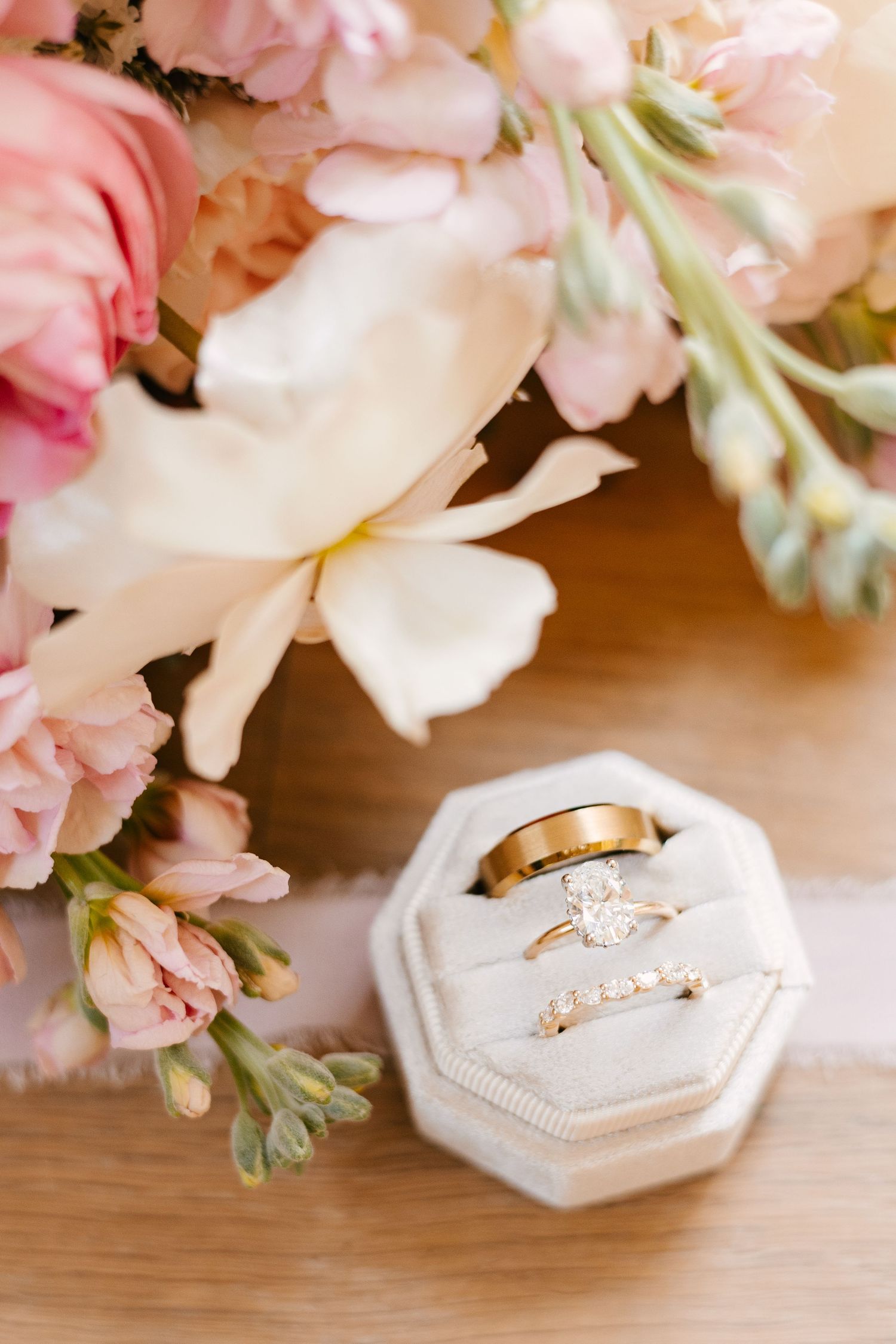 Wedding rings displayed in white hexagonal boxes with soft pink floral arrangements.