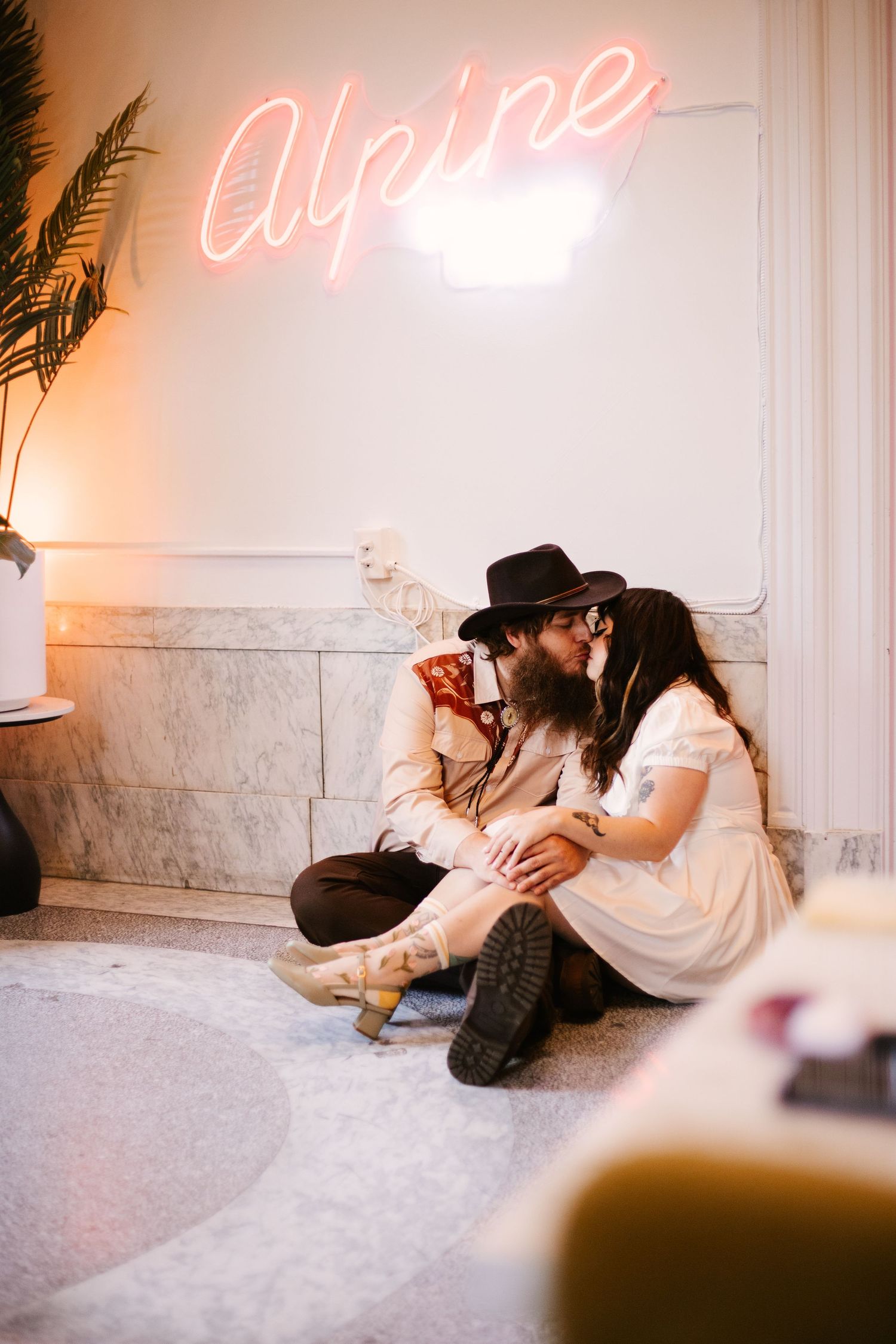 Indoor photoshoot with neon lighting showing couple lounging on white carpet.
