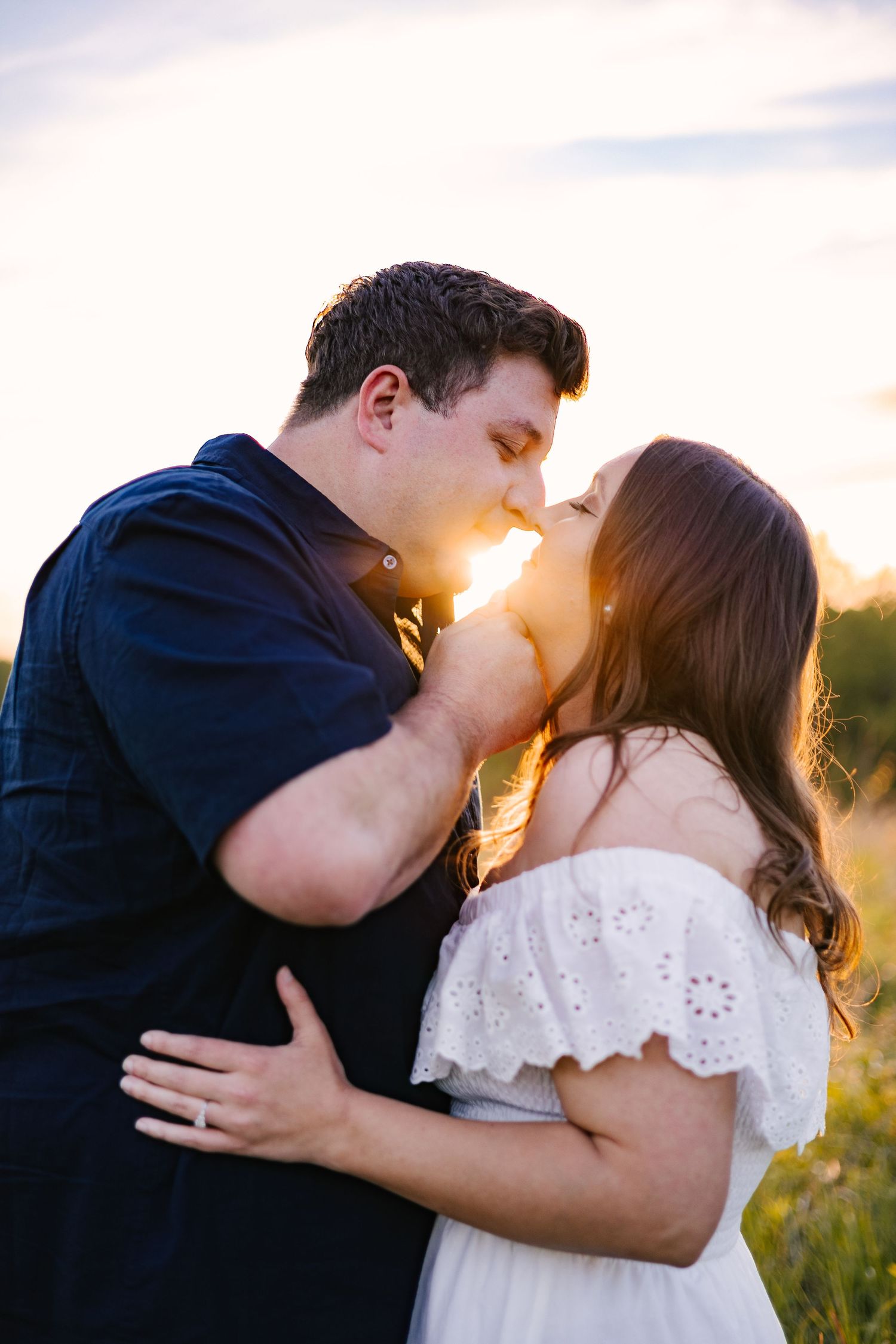 Romantic couple sharing intimate kisses in a golden sunset field with soft backlighting.