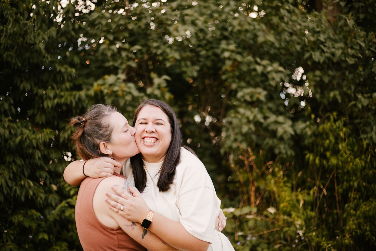 Two friends sharing a warm embrace and laughing in a garden setting.