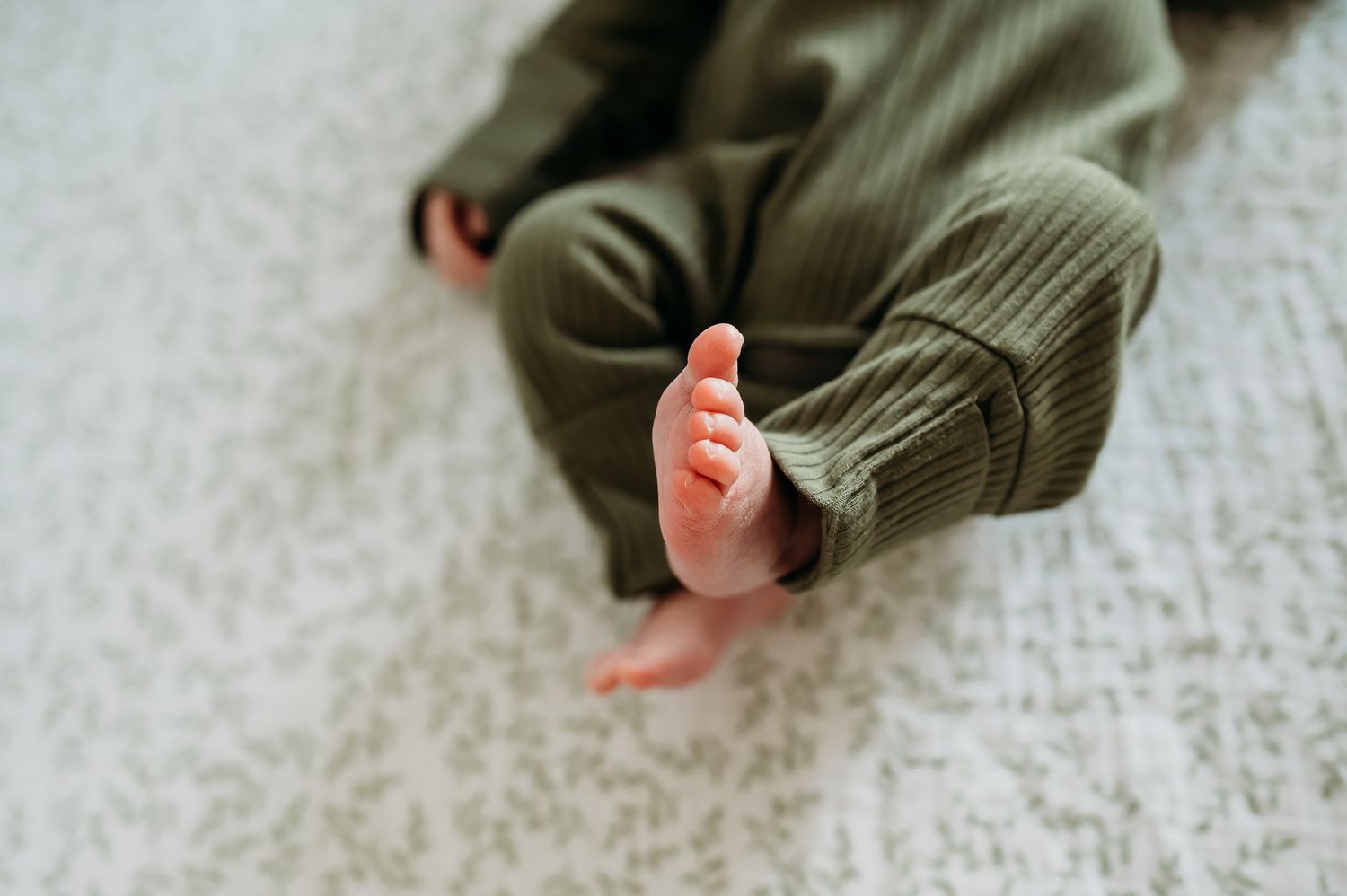 Close-up view of tiny baby feet wrapped in cozy green knit clothing on white carpet background.