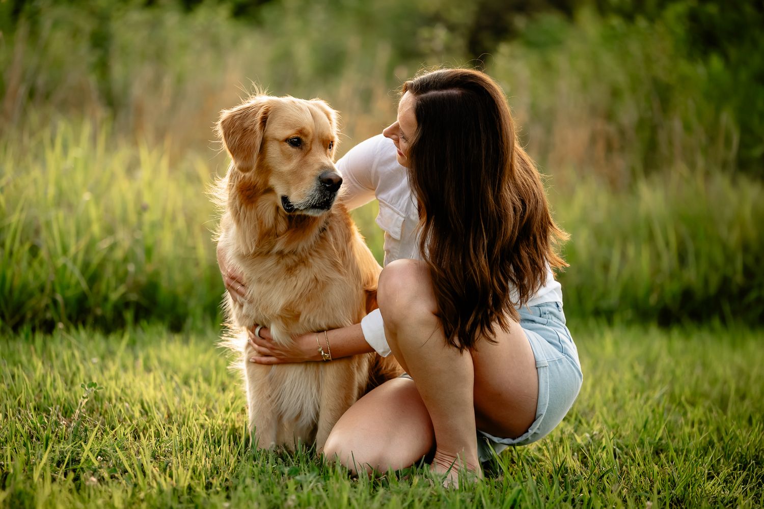 A young woman with long brown hair sits on green grass hugging a golden retriever dog during dog photo session at Hummel Park in Plainfield.