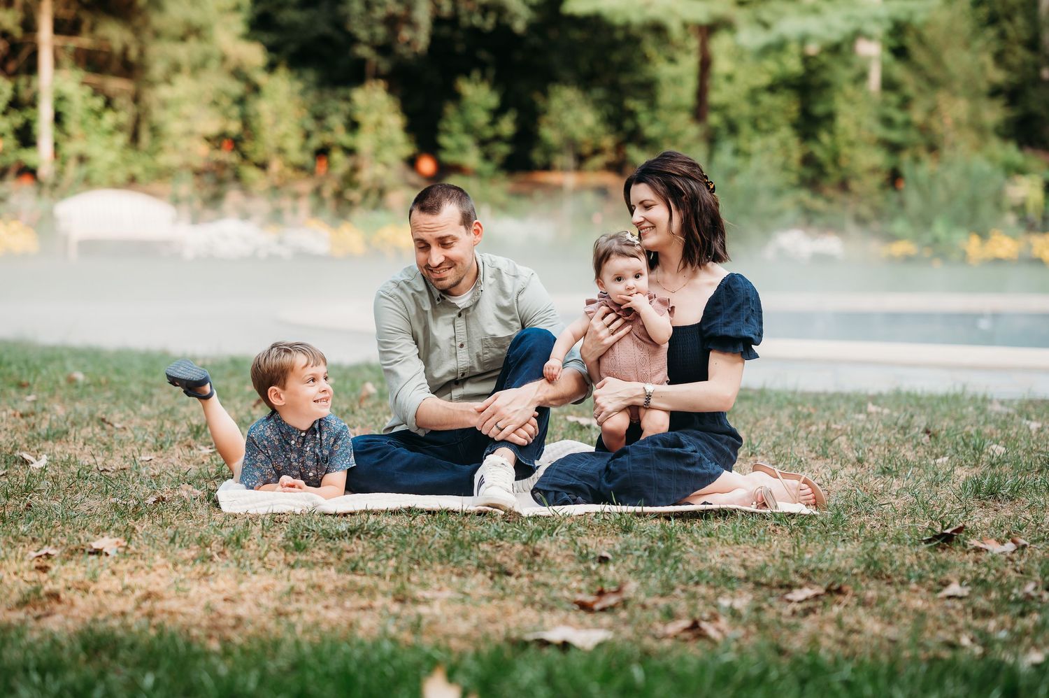 Family lying together on a blanket outdoors in front of fountain at Newfields in Indianapolis.