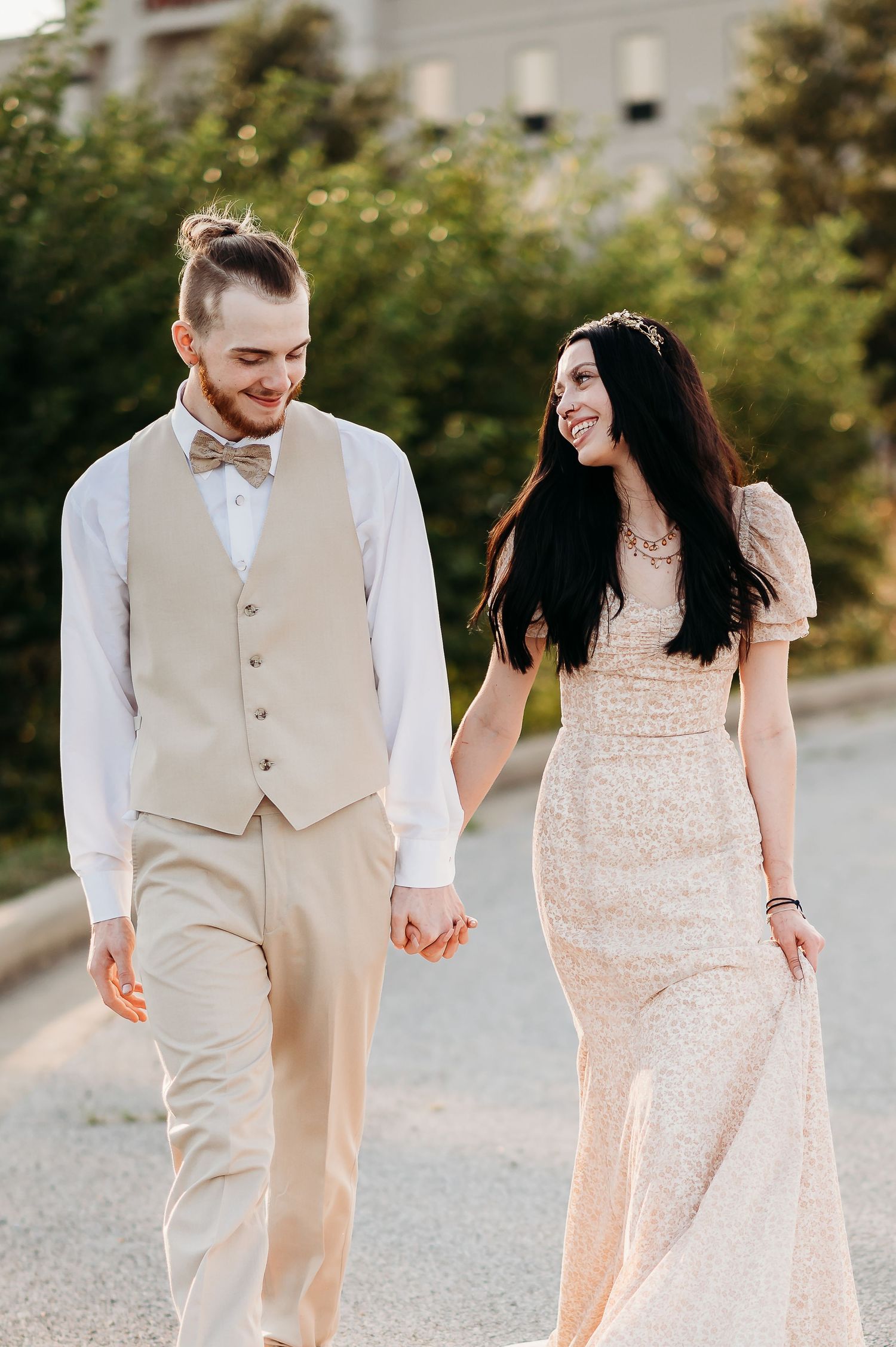 Couple walking together outdoors, bride in lace dress and groom in tan vest and bowtie.