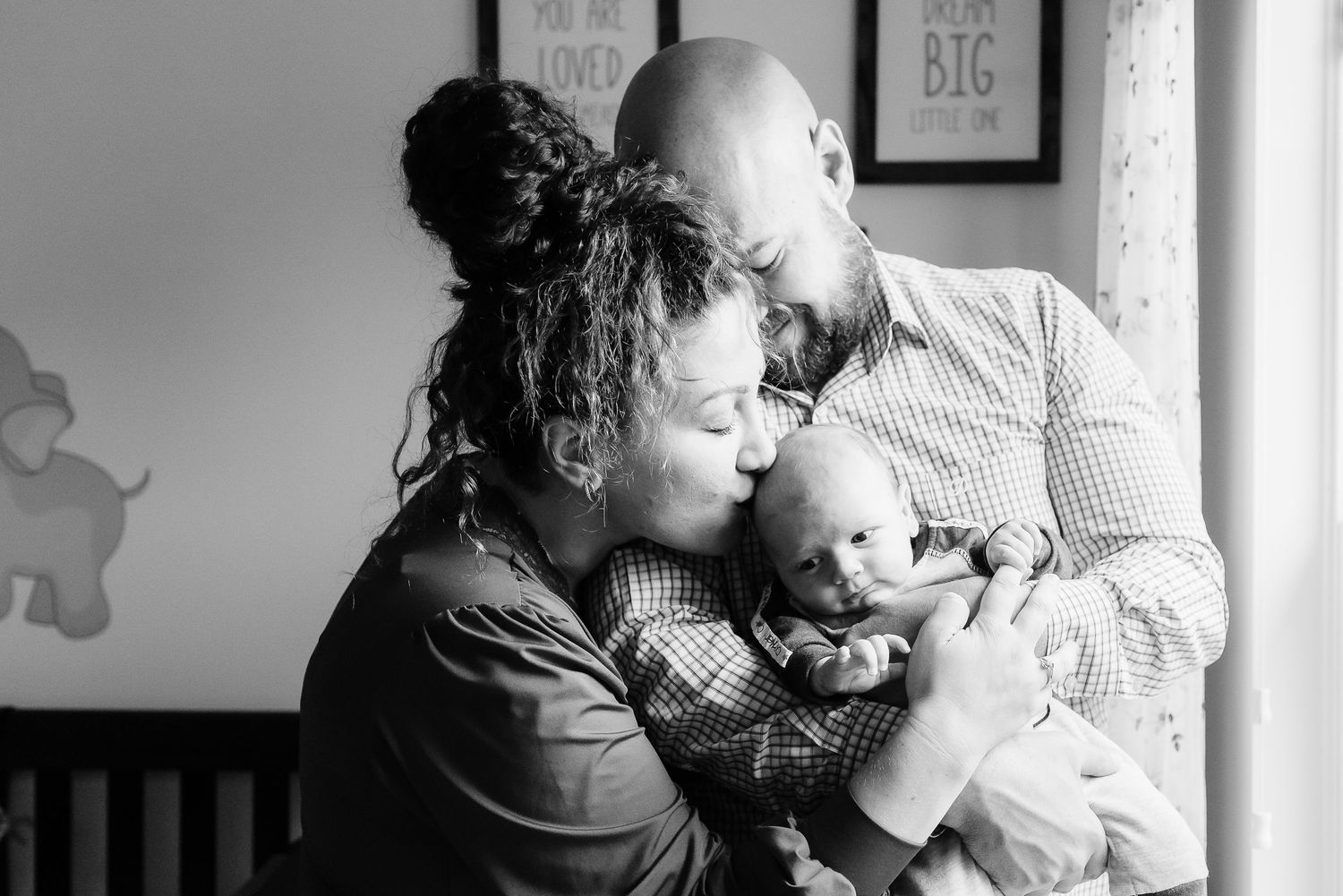 A black and white photograph shows tender moment between parents and baby boy during newborn photos at Avon, Indiana, home.