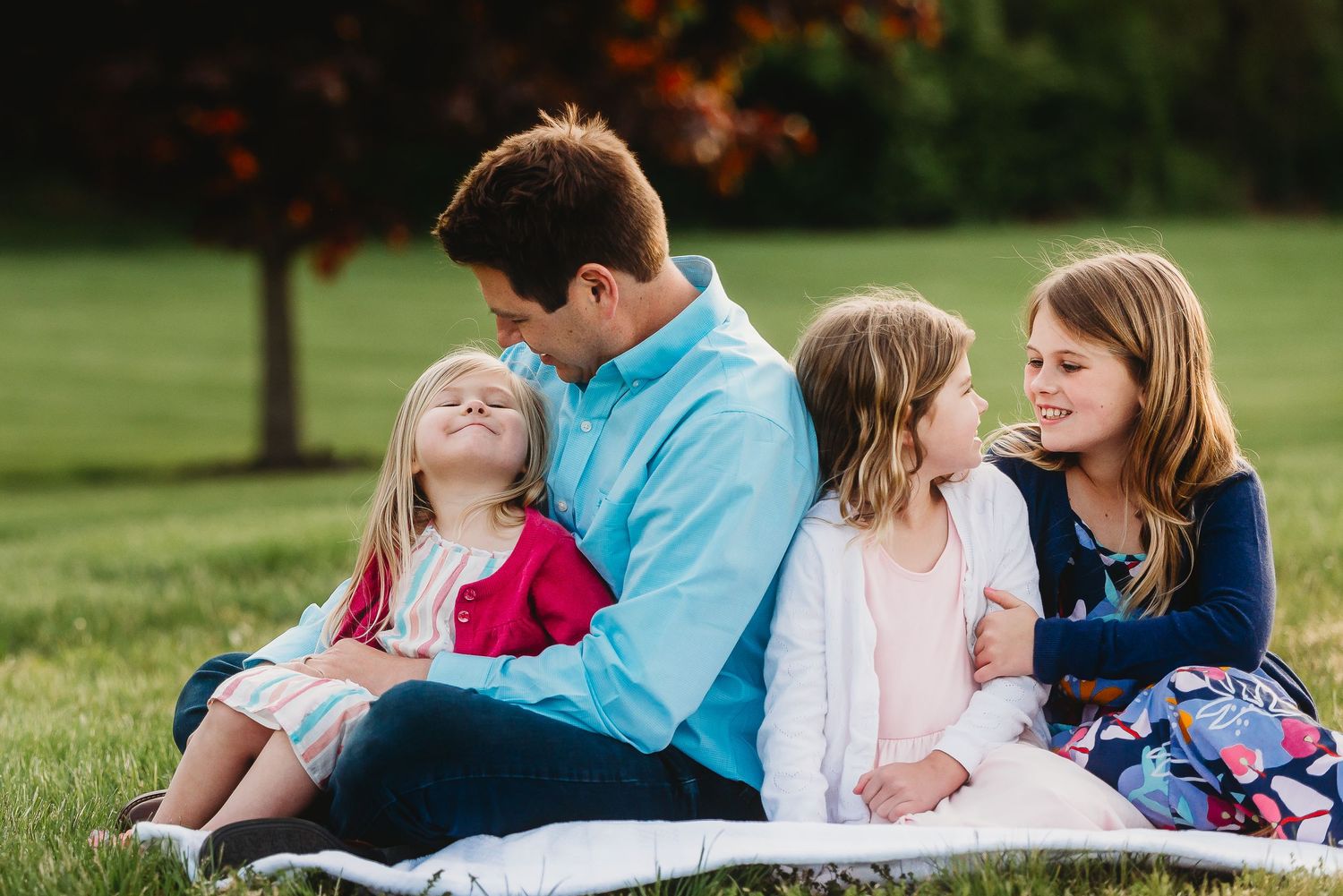Family relaxes together on grass during outdoor photo session at sunset in Friendship Gardens in Plainfield, Indiana.