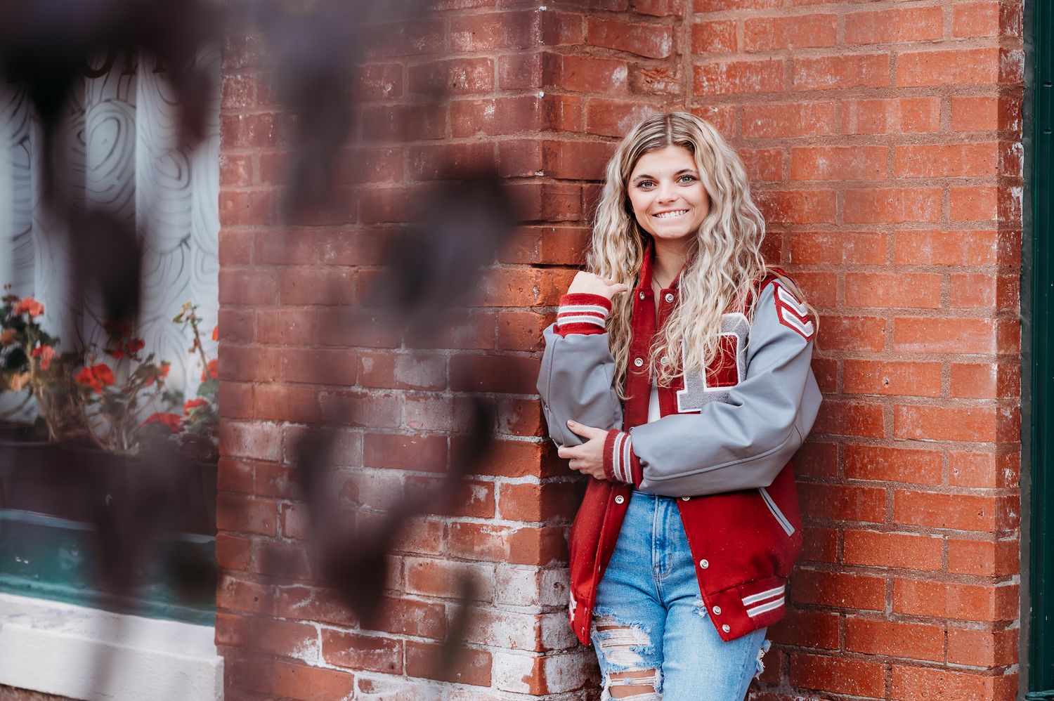 A person wearing a varsity jacket and jeans leans against a brick wall in a casual outdoor portrait.