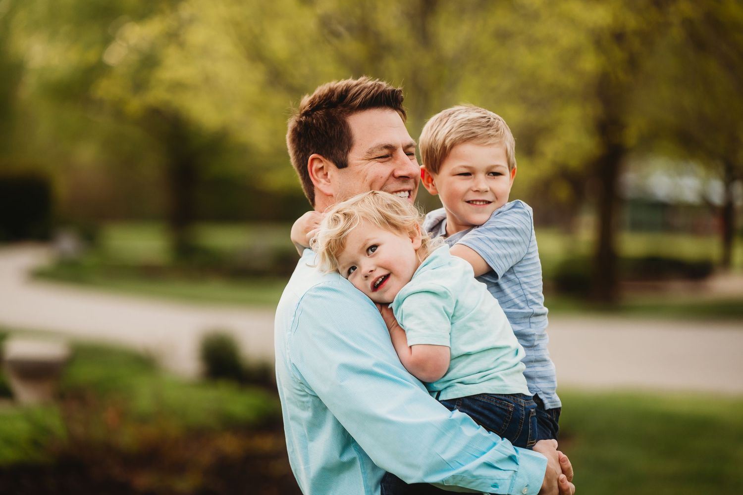 Dad and two little boys share joyful laughter while embracing outdoors during spring photo session in Plainfield, Indiana.