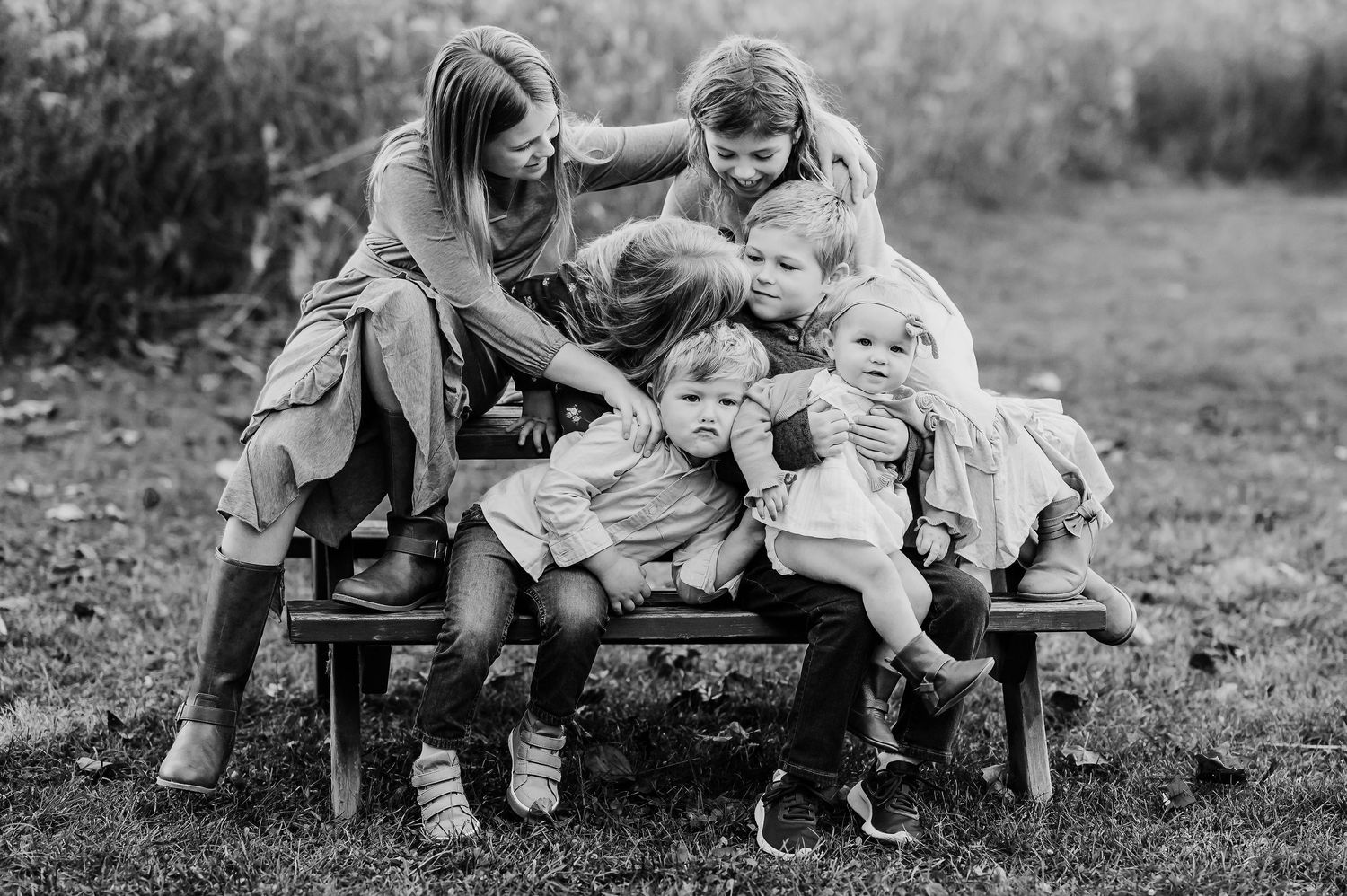 A black and white candid photo showing six children sitting on a bench for Fall Family Photos at Ritchey Woods Nature Preserve Fishers, IN.