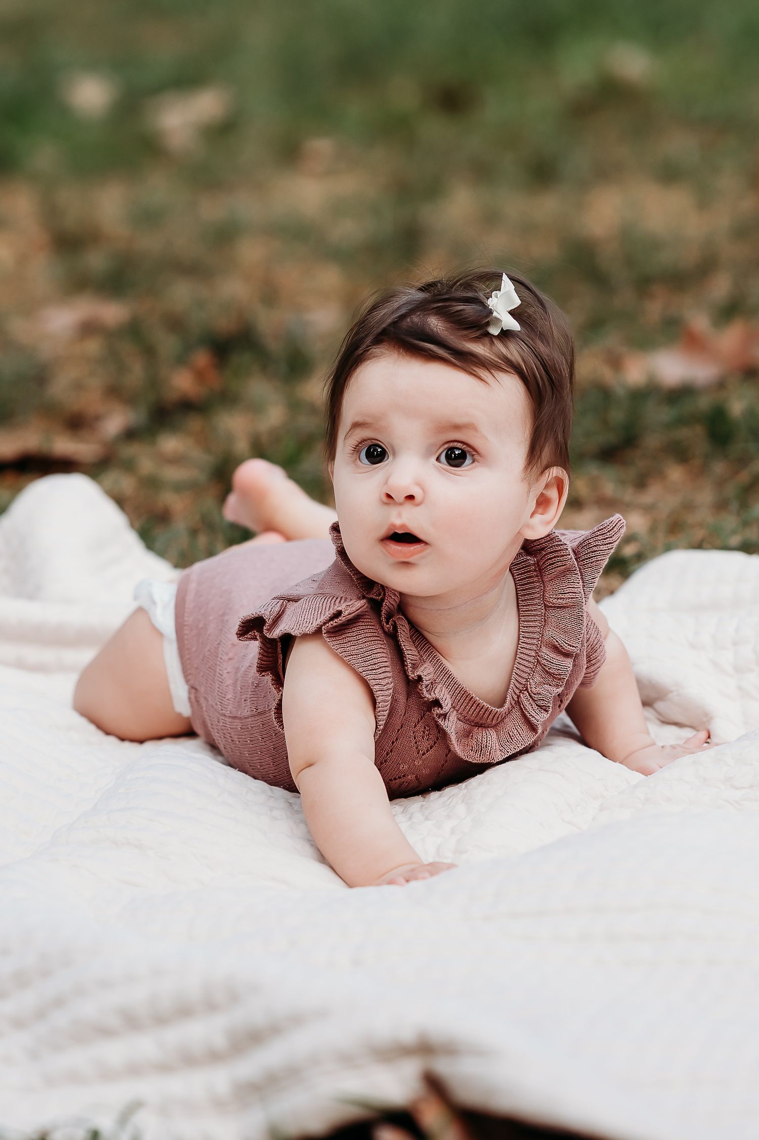 A baby in a pink ruffled outfit lies on a white blanket outdoors at Newfields during an Indianapolis family photo session..