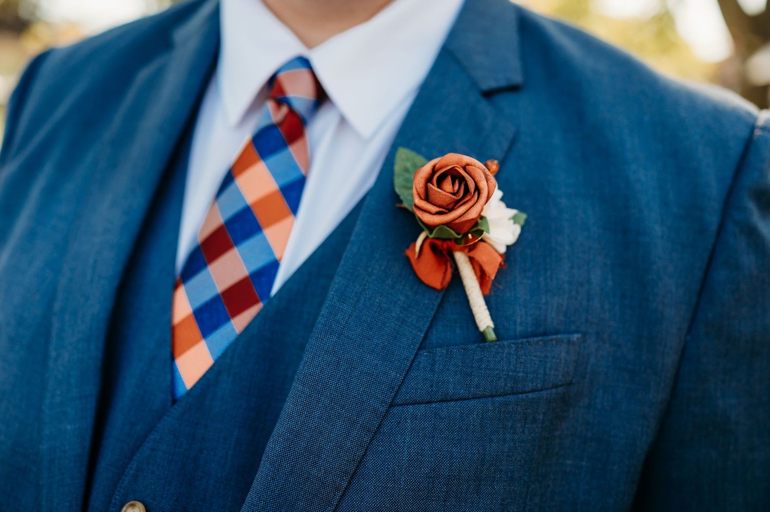 Navy blue suit with orange and blue striped tie accented by a delicate orange rose boutonniere.