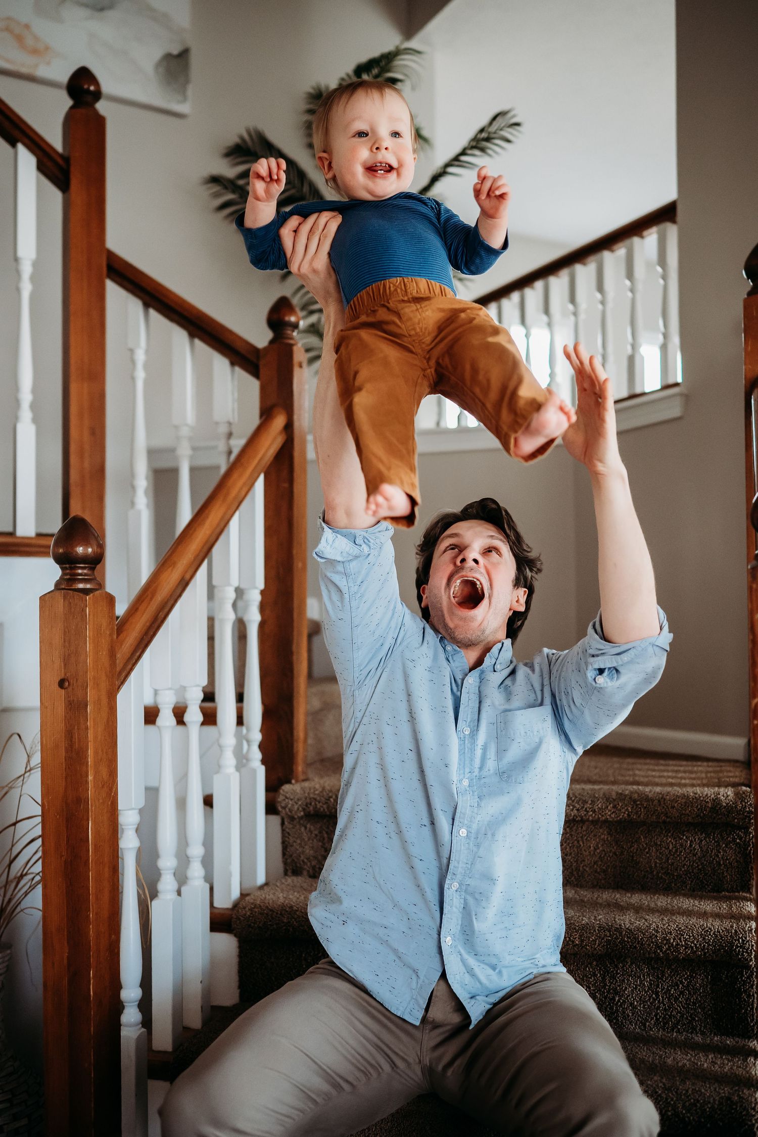A joyful father lifts his laughing toddler high in the air on a carpeted staircase inside a cozy Indianapolis home.
