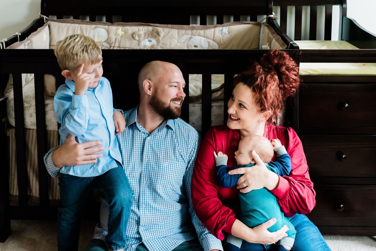 Family in coordinating blue and red outfits sharing tender moments during a newborn photo session at home in Avon, Indiana.